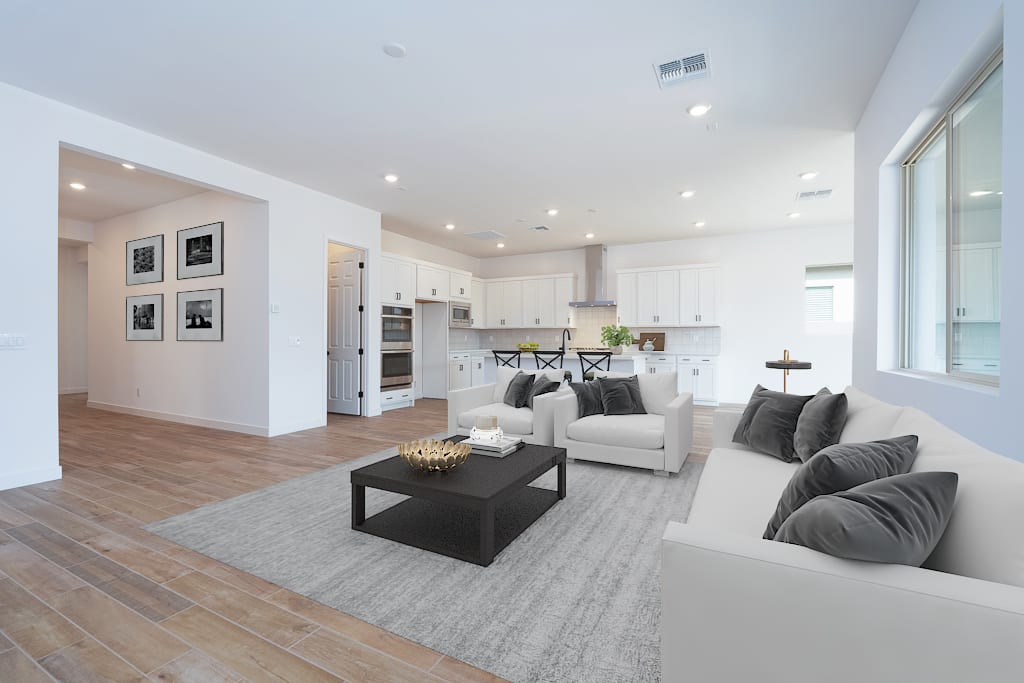 A modern, open-concept living space with a white kitchen, gray sofas, and a wooden floor in the foreground, leading to a bright and airy atmosphere in the background.