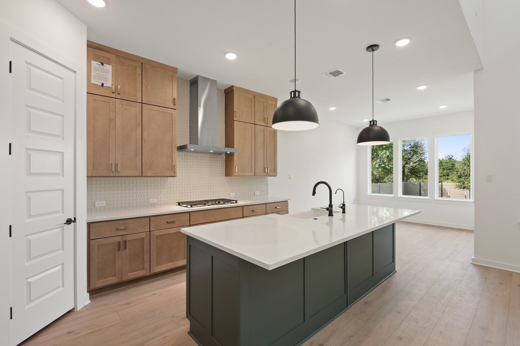 A modern and spacious kitchen with light wood cabinets, a large island with a white countertop, and pendant lights hanging above.
