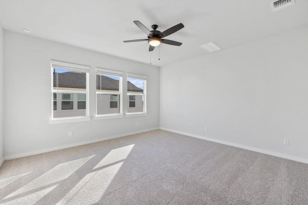 An empty bedroom with a ceiling fan, large windows, and gray carpeted floor.
