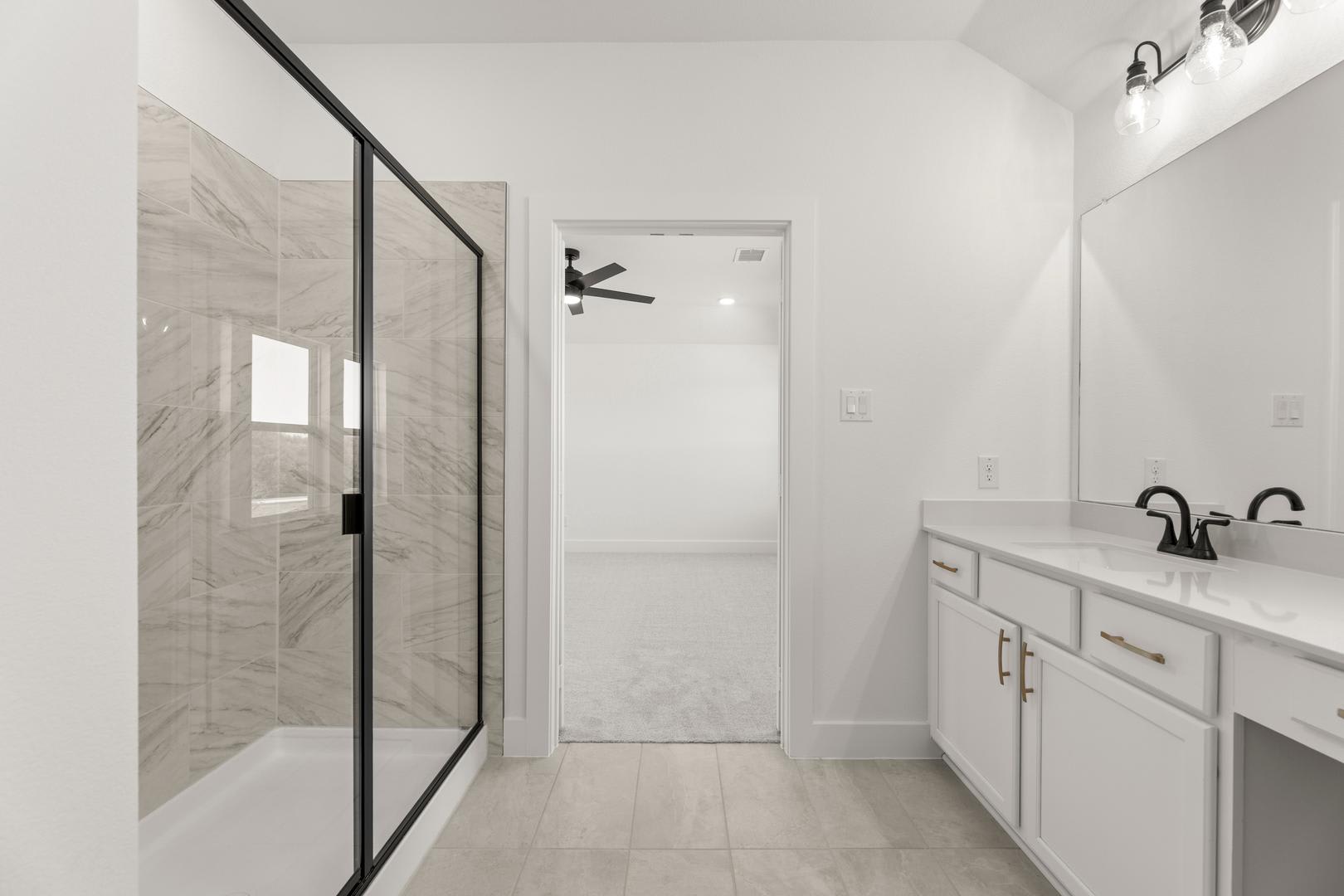 A modern, minimalist bathroom with a glass-enclosed shower, white cabinets, and a tiled floor.