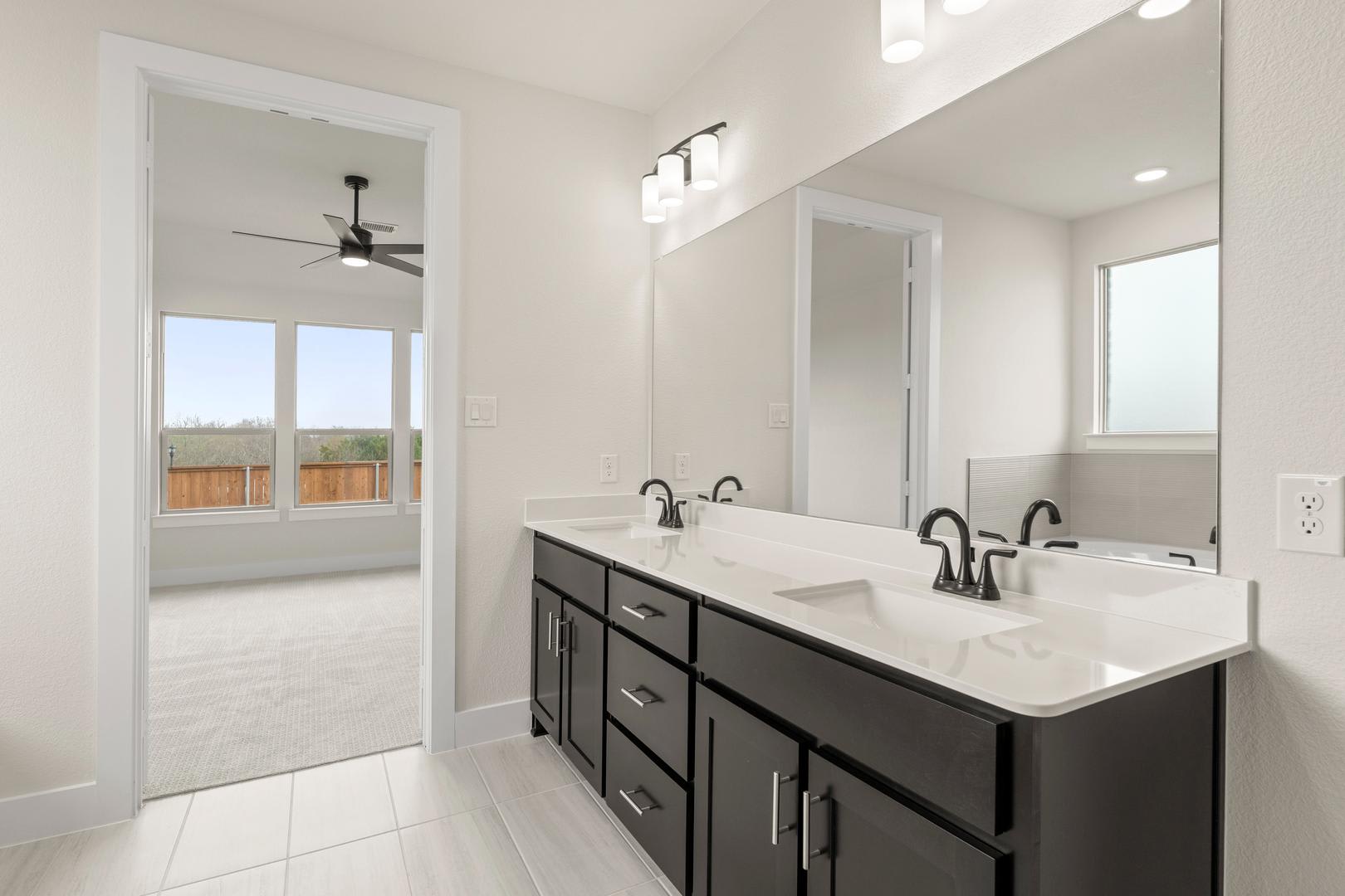A modern and spacious bathroom with a double vanity, dark cabinets, and a window overlooking the outdoor area.