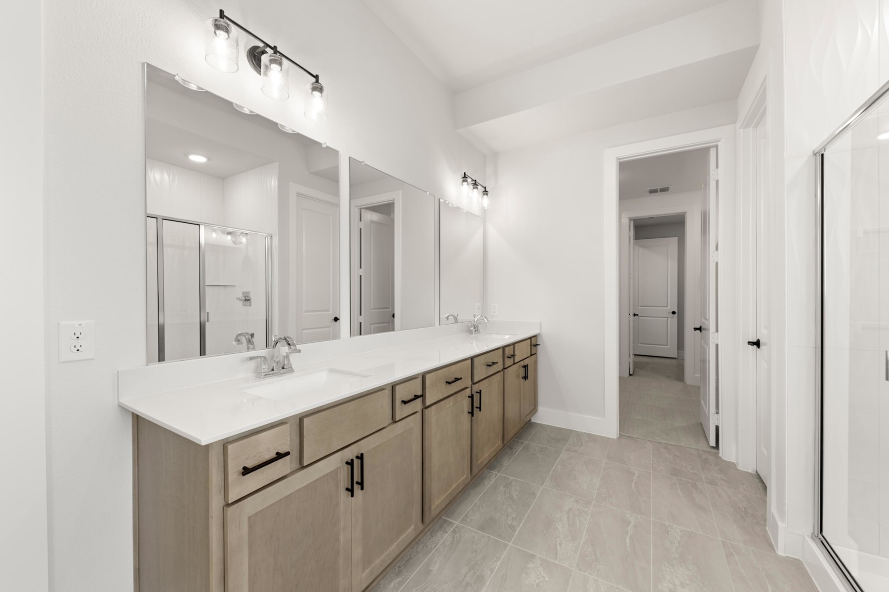 A spacious and modern bathroom with a large vanity, white countertops, and a tiled floor leading to an open doorway.