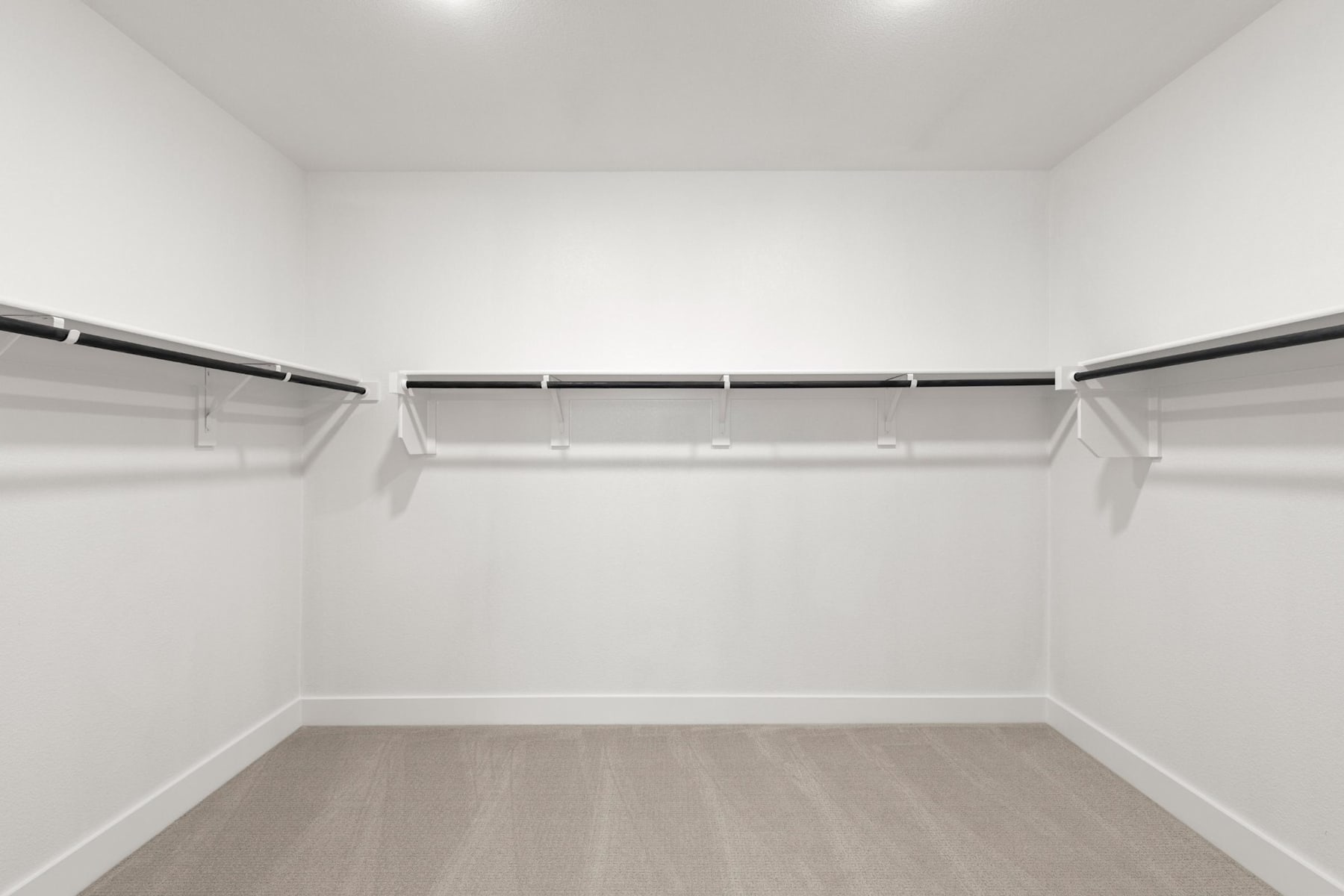 A spacious, well-lit closet with white walls, a wooden floor, and multiple hanging rods for storing clothes.
