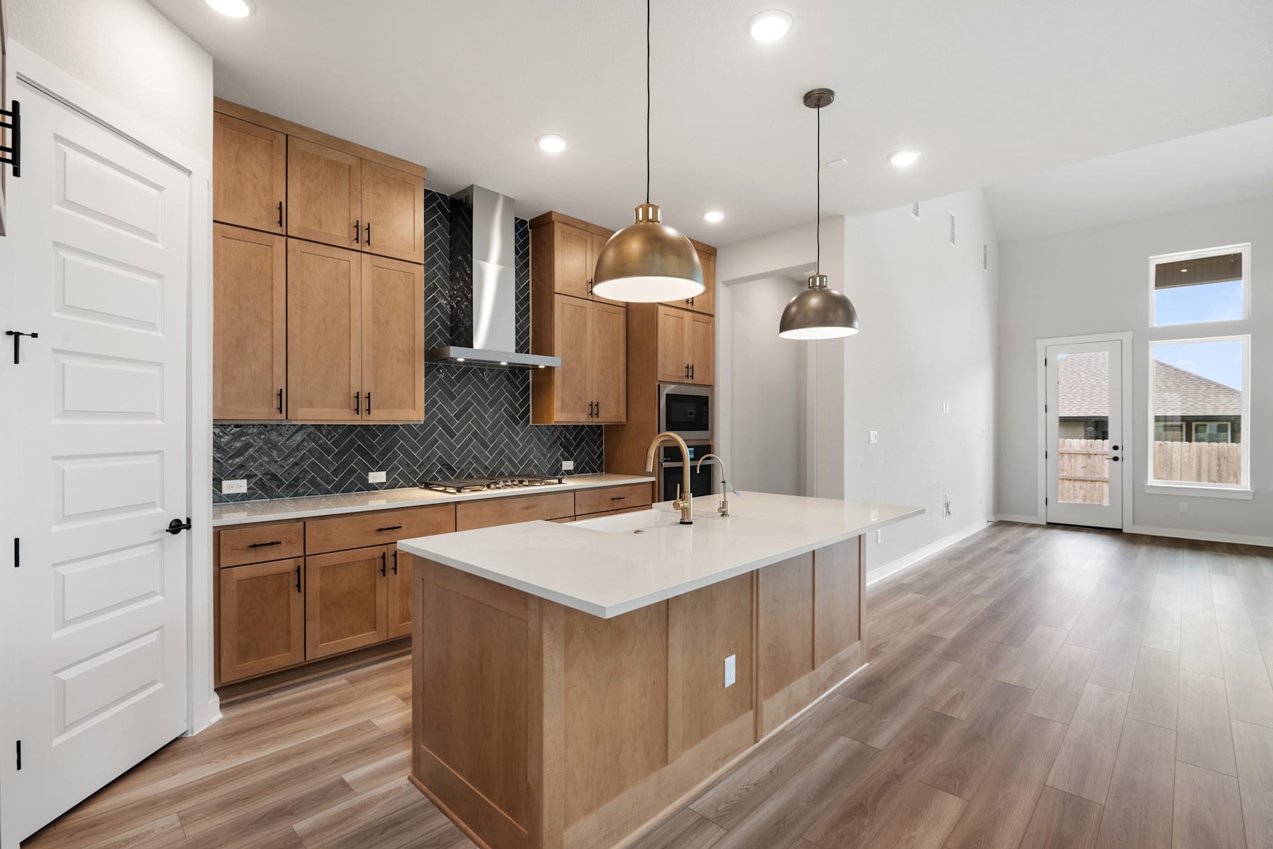 A modern and spacious kitchen with wooden cabinets, a white countertop, and pendant lighting fixtures, set against a backdrop of hardwood floors and a white wall.