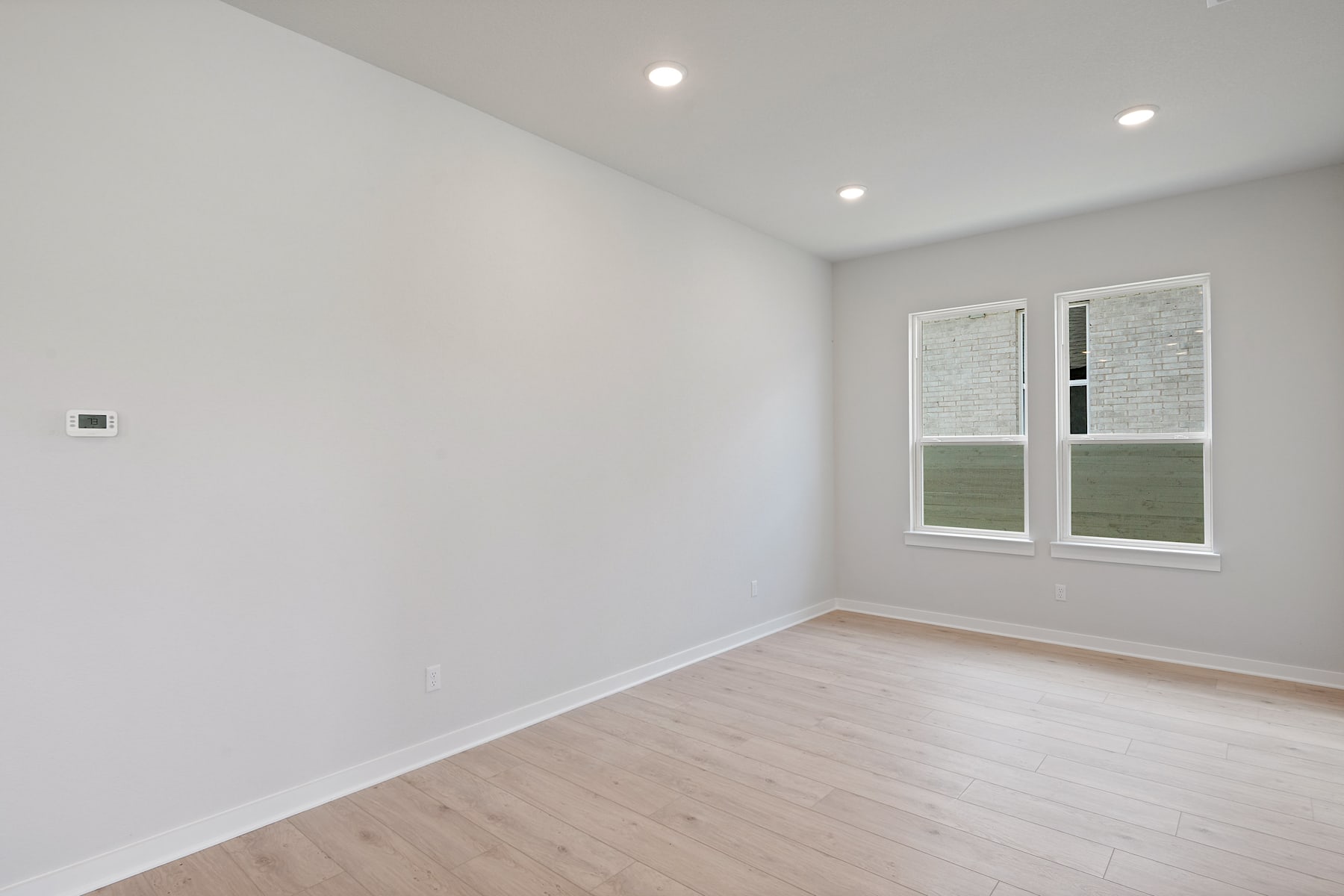 A bright, minimalist room with white walls, a large window, and a hardwood floor.