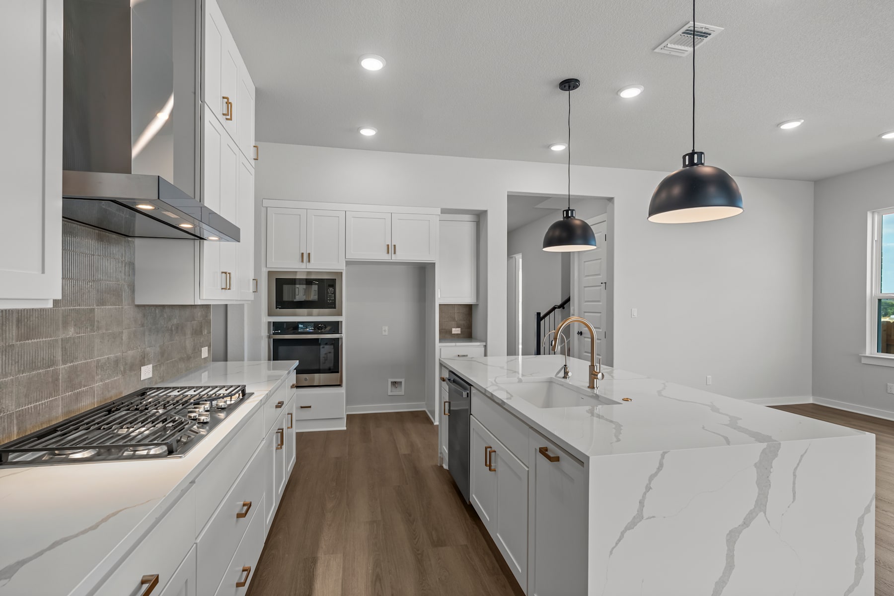 A modern, well-lit kitchen with white cabinets, gray countertops, and pendant lights hanging above the island.