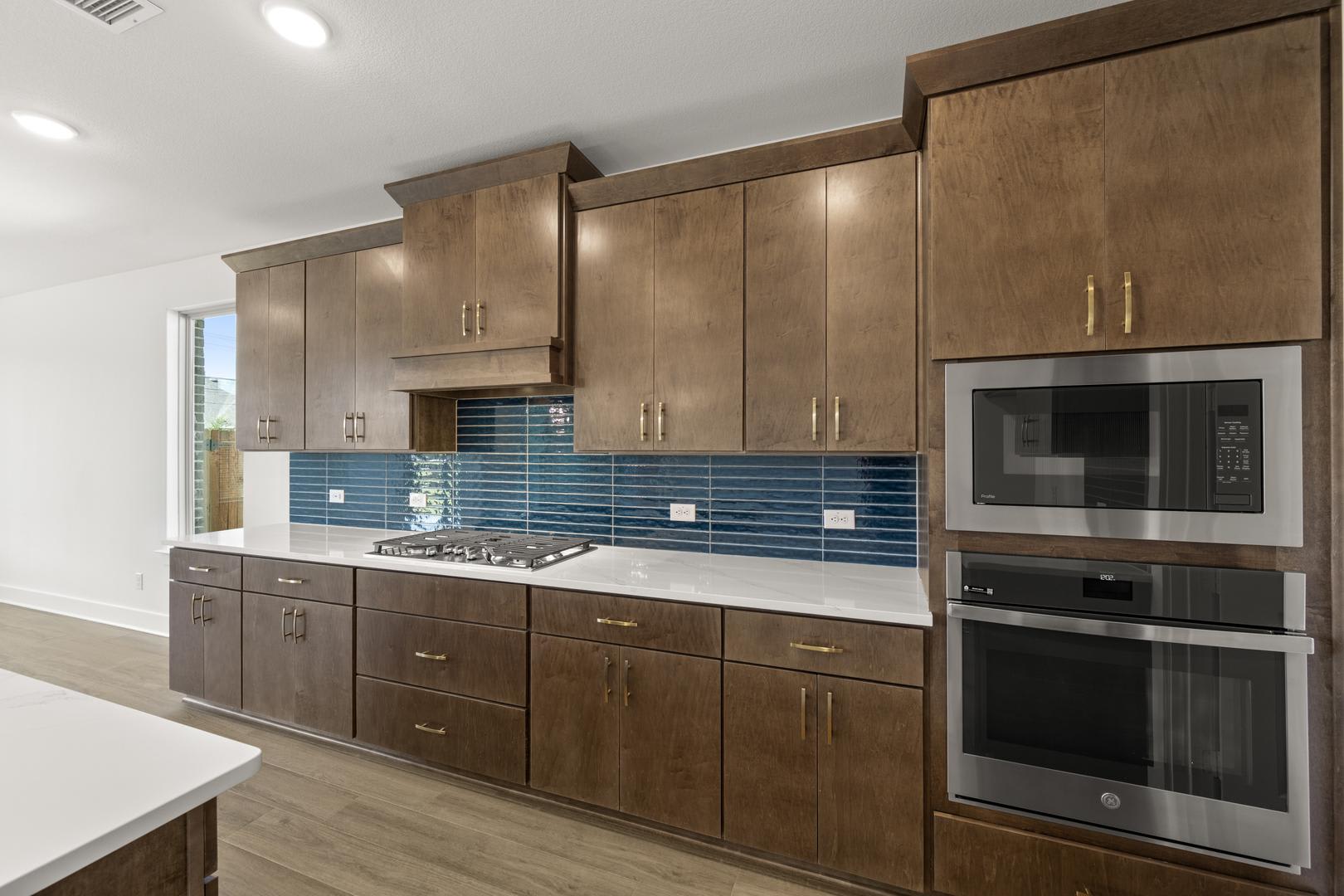 A modern and well-equipped kitchen with wooden cabinets, stainless steel appliances, and a backsplash of blue tiles, set against a bright and airy background.
