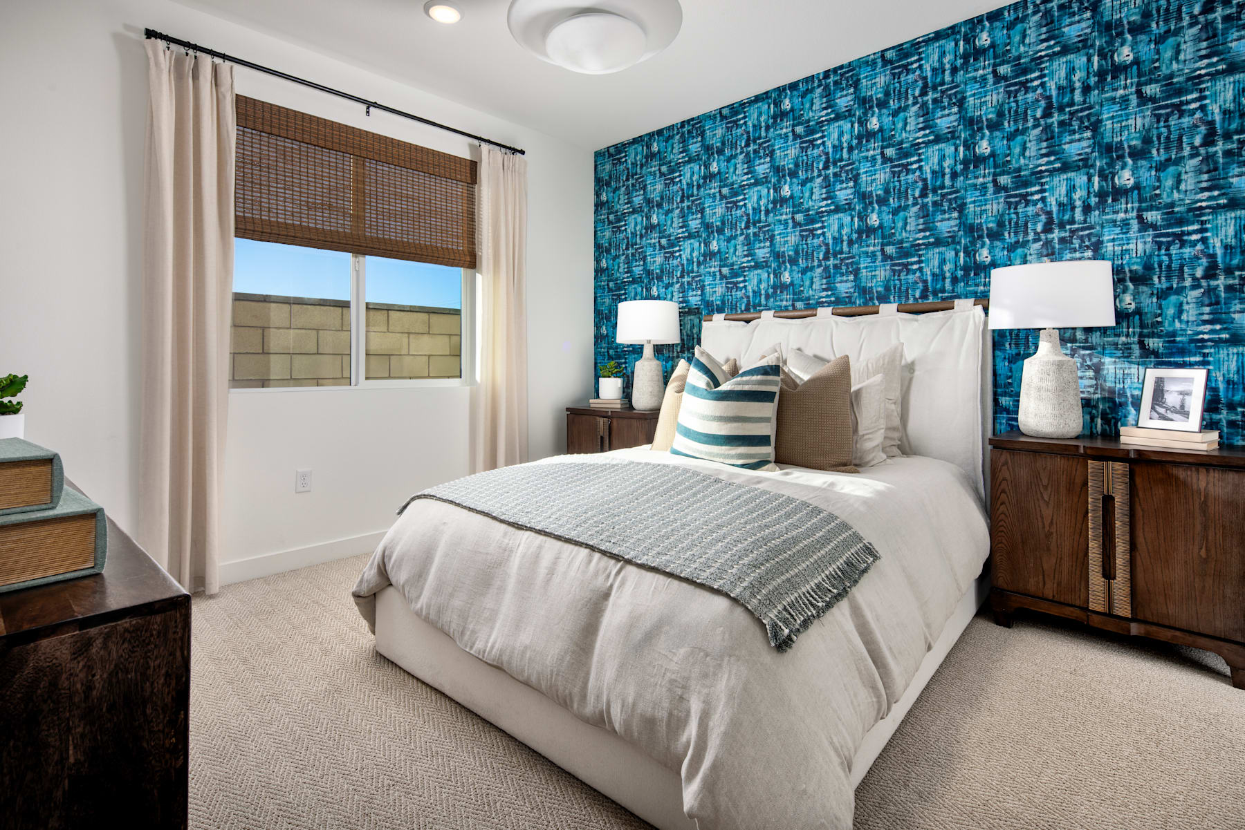 A cozy and modern bedroom with a patterned blue accent wall, a white bed with decorative pillows, and wooden nightstands on either side.