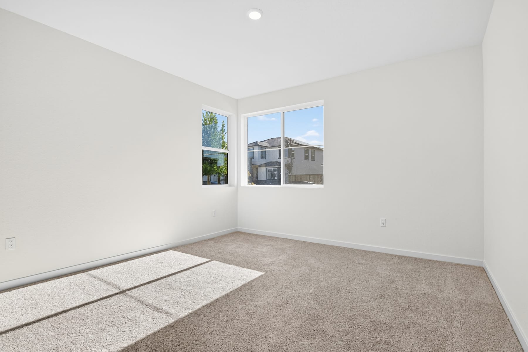 A bright, empty room with a large window overlooking a residential neighborhood in the background.