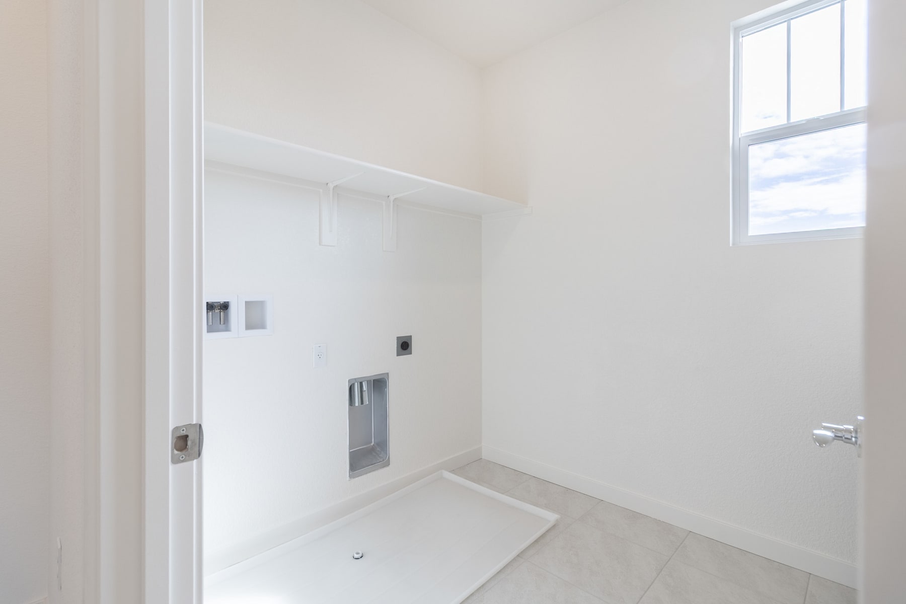 A bright, minimalist interior with a white wall, a window, and a tiled floor in the foreground.
