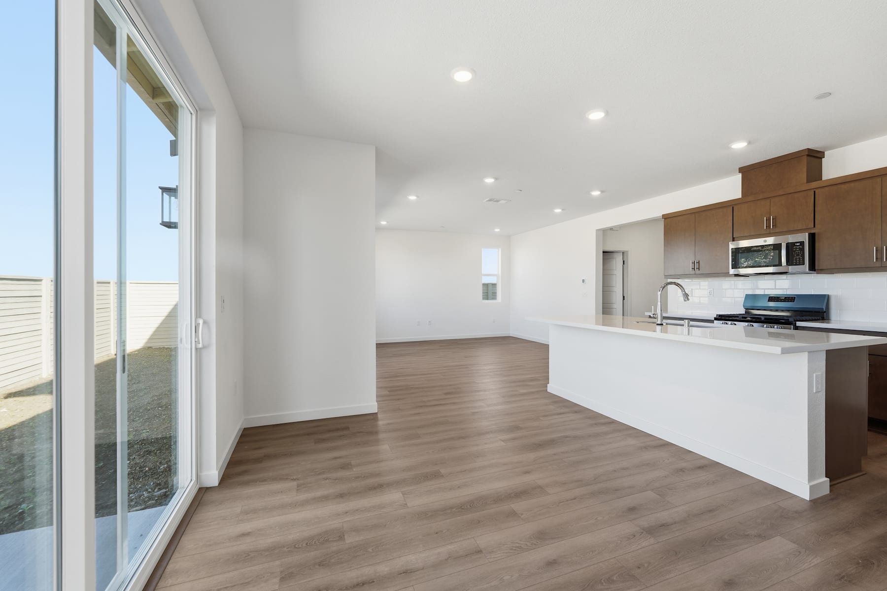 A modern, open-concept kitchen and living space with white walls, wooden floors, and large windows providing ample natural light.