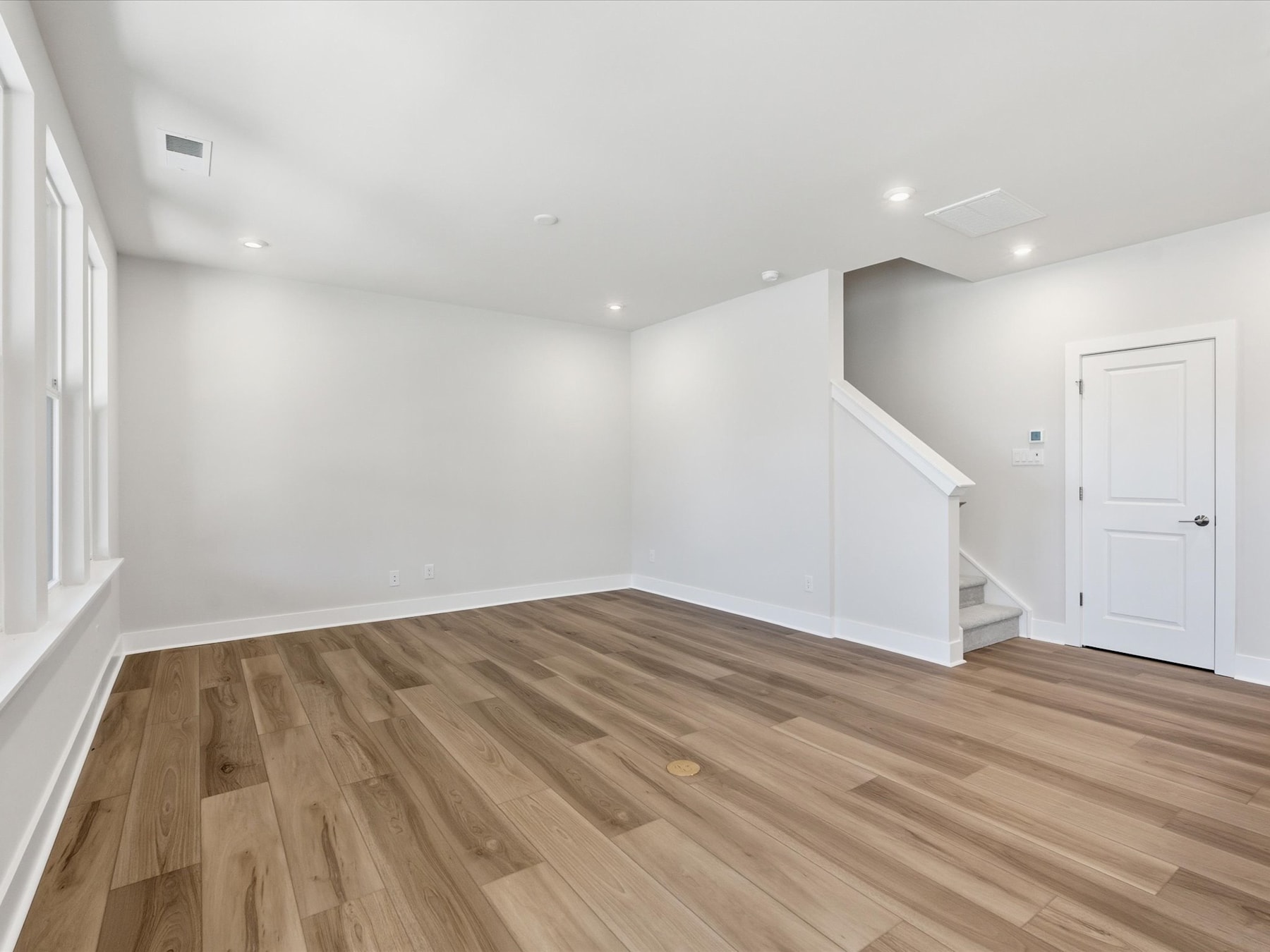 A spacious, well-lit room with white walls and a hardwood floor, featuring a doorway leading to another area.