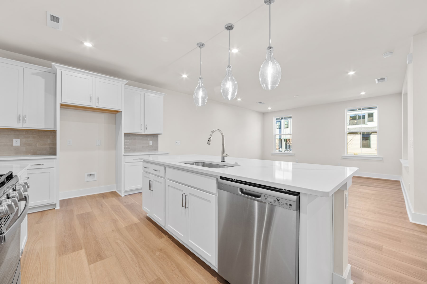 A modern, bright, and spacious kitchen with white cabinets, stainless steel appliances, and pendant lighting fixtures hanging from the ceiling.