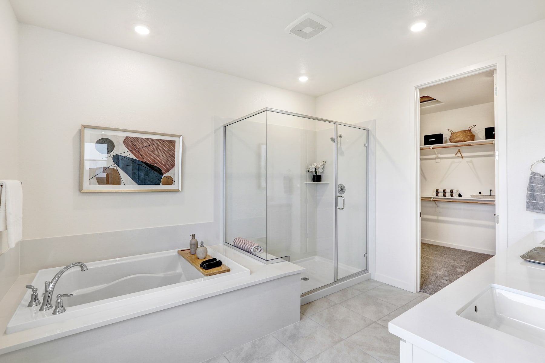 A modern, minimalist bathroom with a large bathtub, glass shower enclosure, and shelving unit visible in the background.