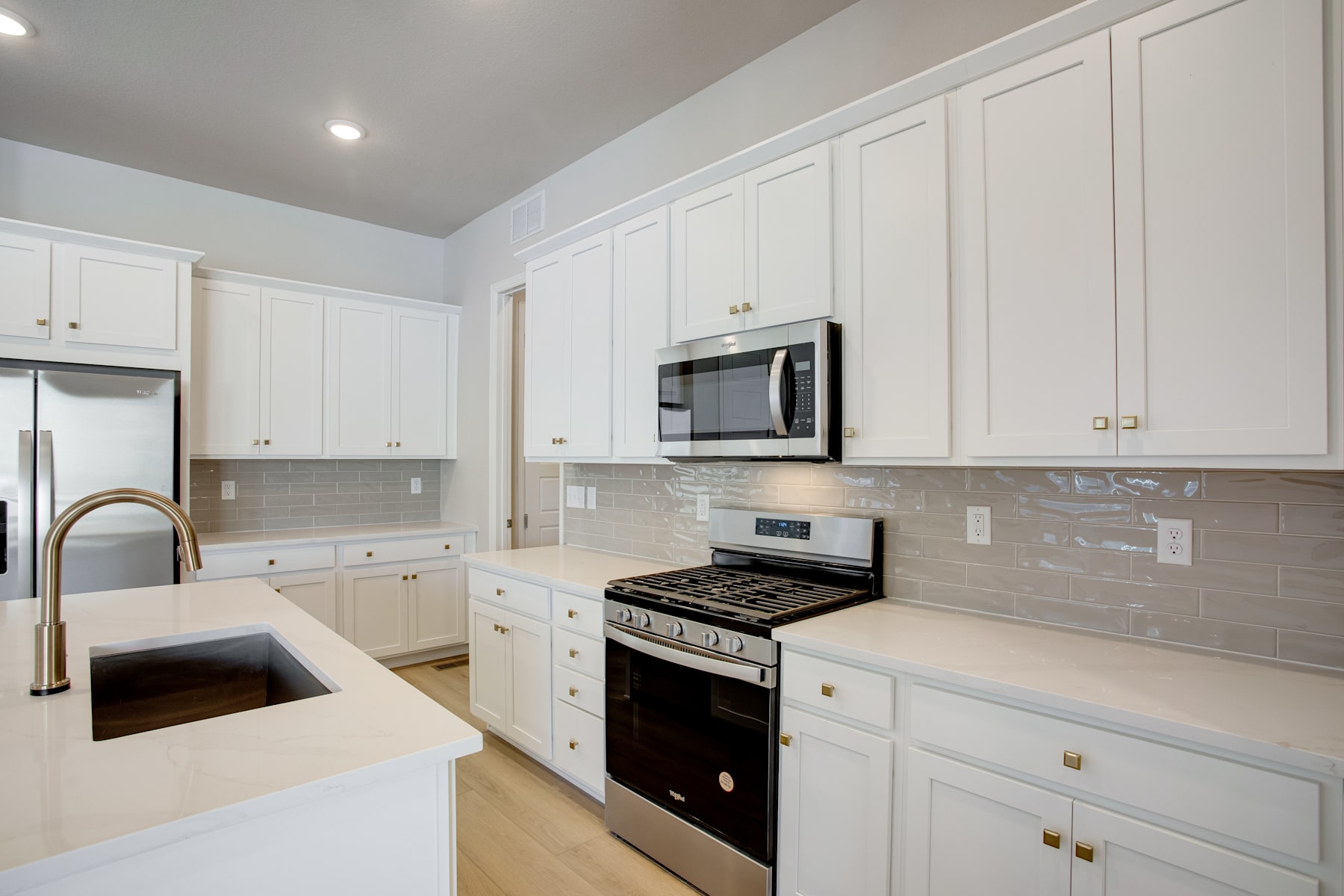 A modern, well-equipped kitchen with white cabinets, a stove, and a microwave oven, set against a neutral-toned backsplash and countertops.