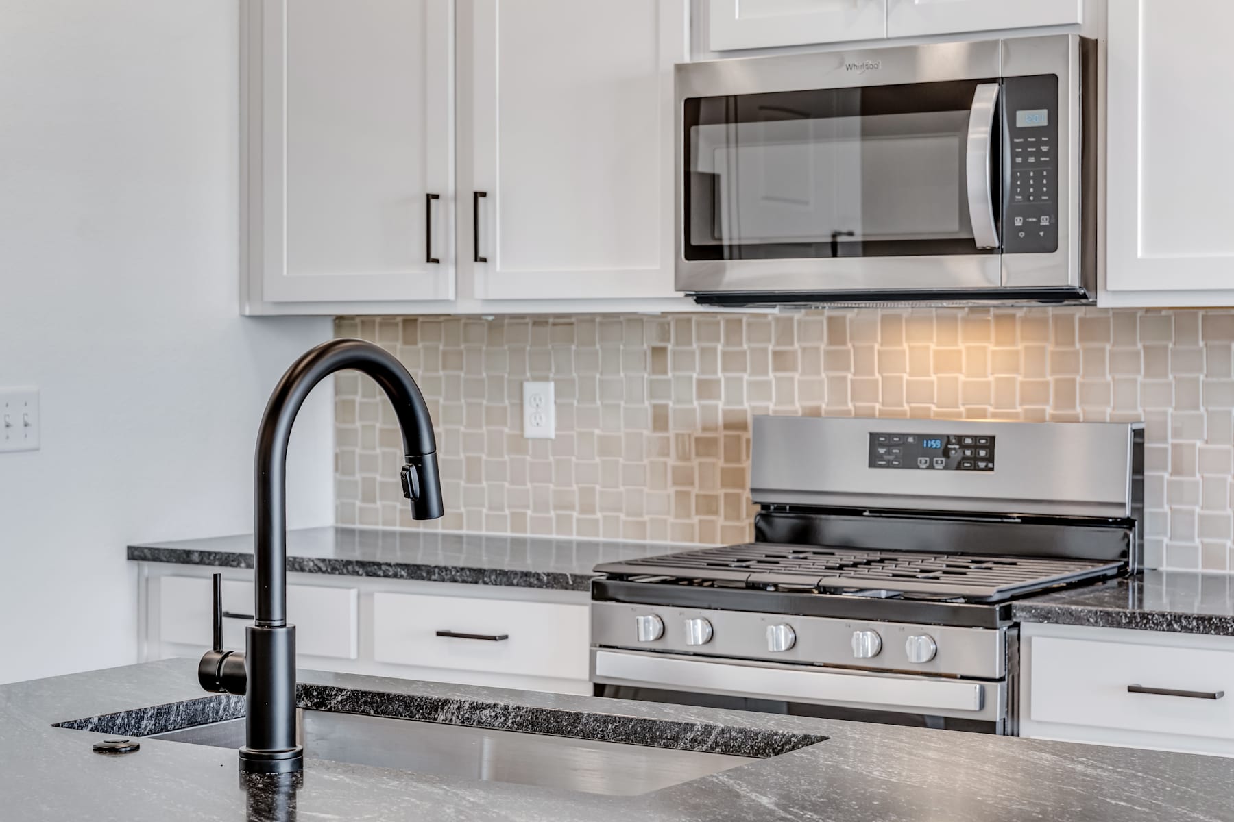 A modern kitchen with white cabinets, a stainless steel oven and microwave, and a granite countertop with a black faucet.