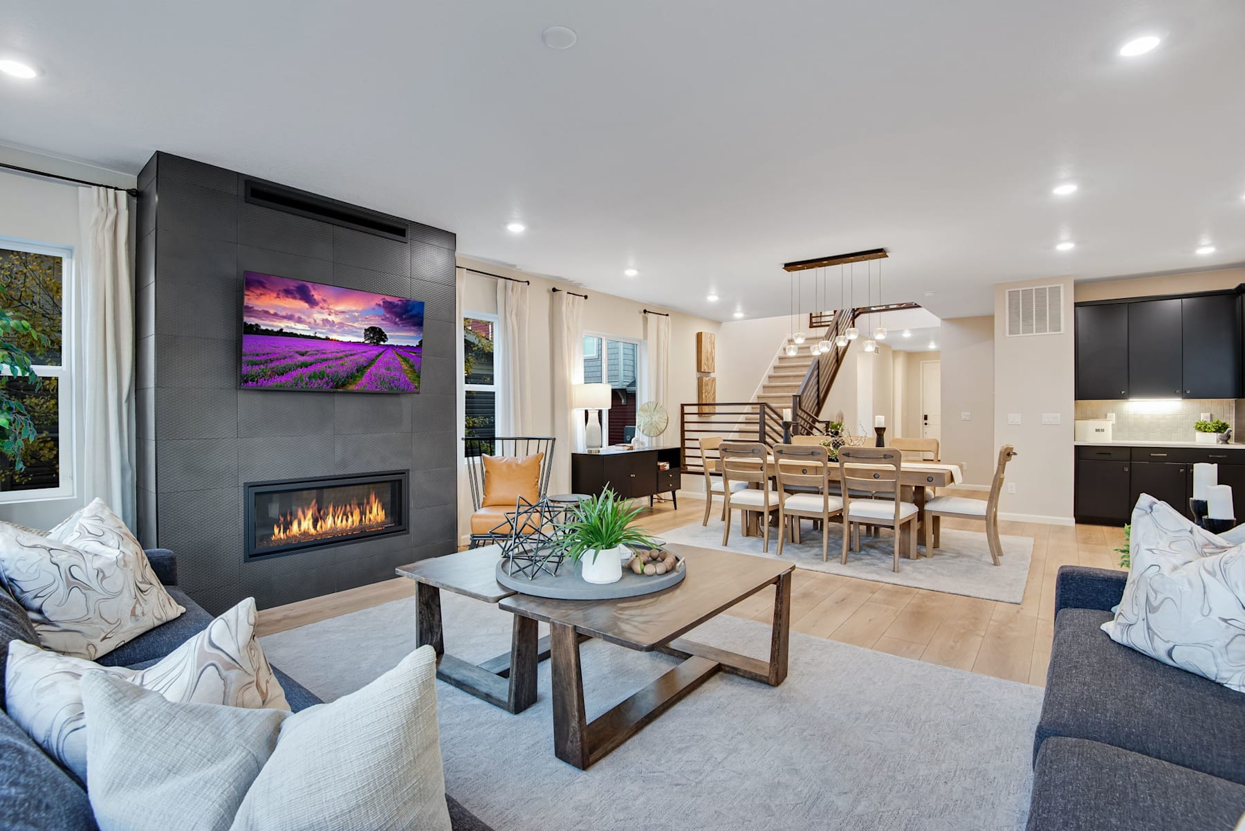 A modern and cozy living room with a fireplace, comfortable seating, and a dining area visible in the background, complemented by artwork on the wall and natural lighting.