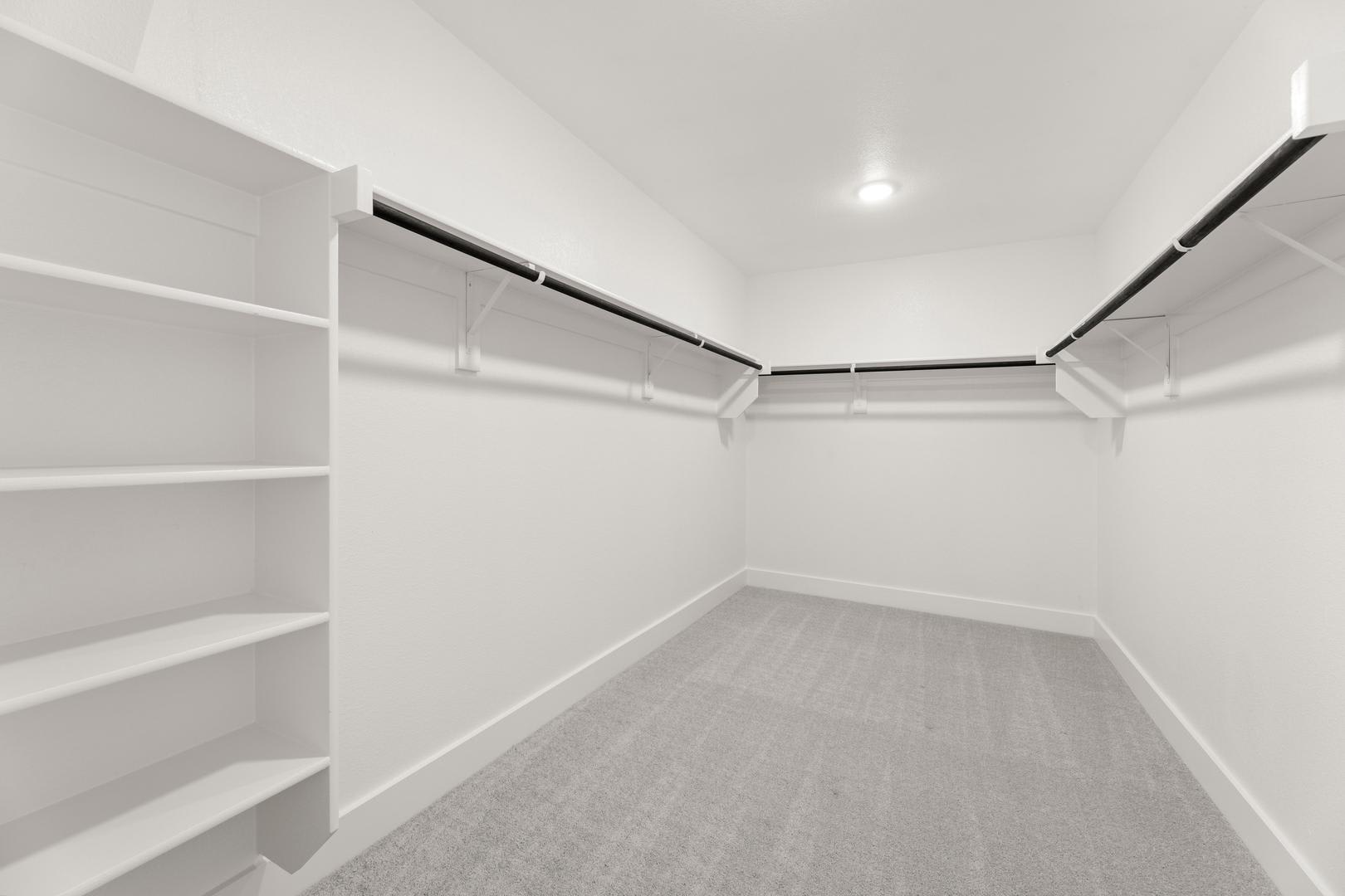 A spacious, well-lit walk-in closet with white shelves and a gray carpeted floor.
