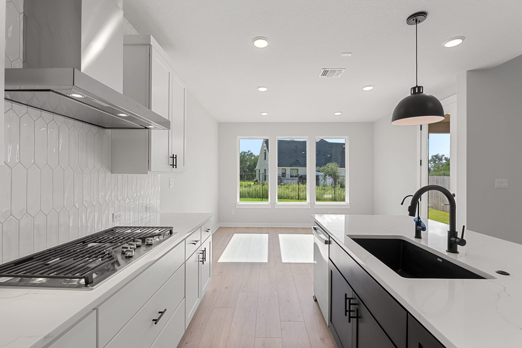 A modern, minimalist kitchen with white cabinets, a gas stove, and large windows overlooking a scenic outdoor landscape.