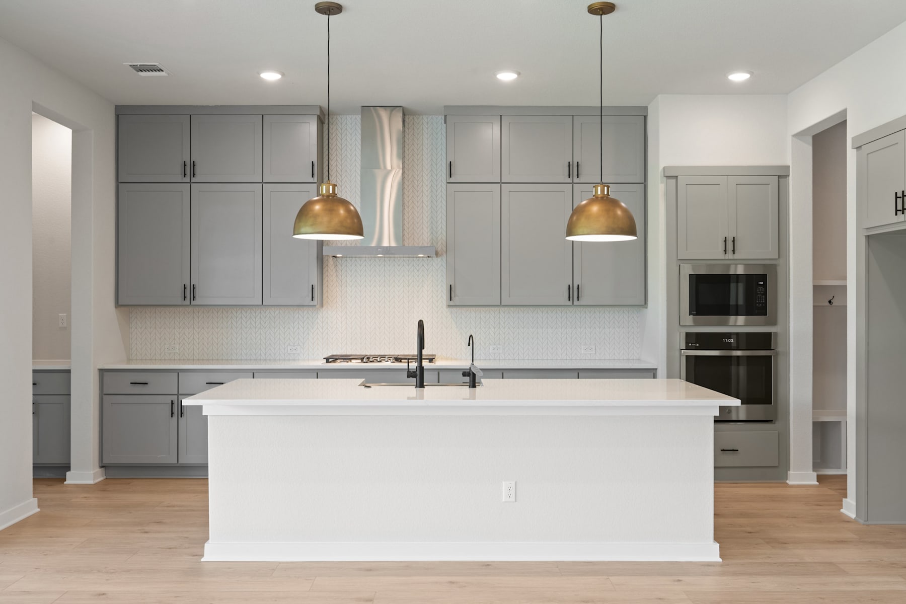 A modern, minimalist kitchen with gray cabinets, white countertops, and gold pendant lights, featuring an island in the foreground.