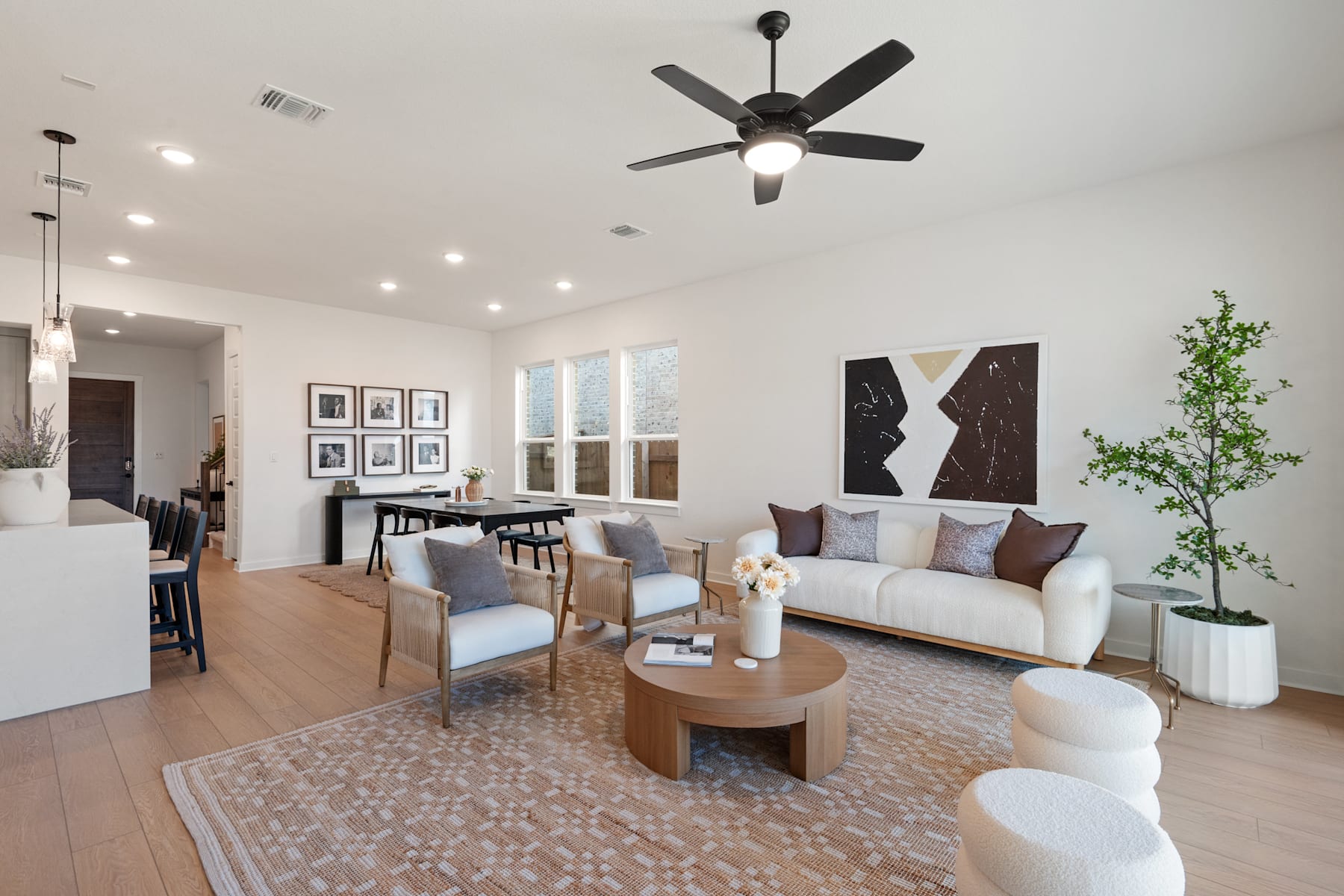 A modern and stylish living room with a ceiling fan, artwork on the walls, and a cozy seating arrangement around a wooden coffee table on a patterned rug.