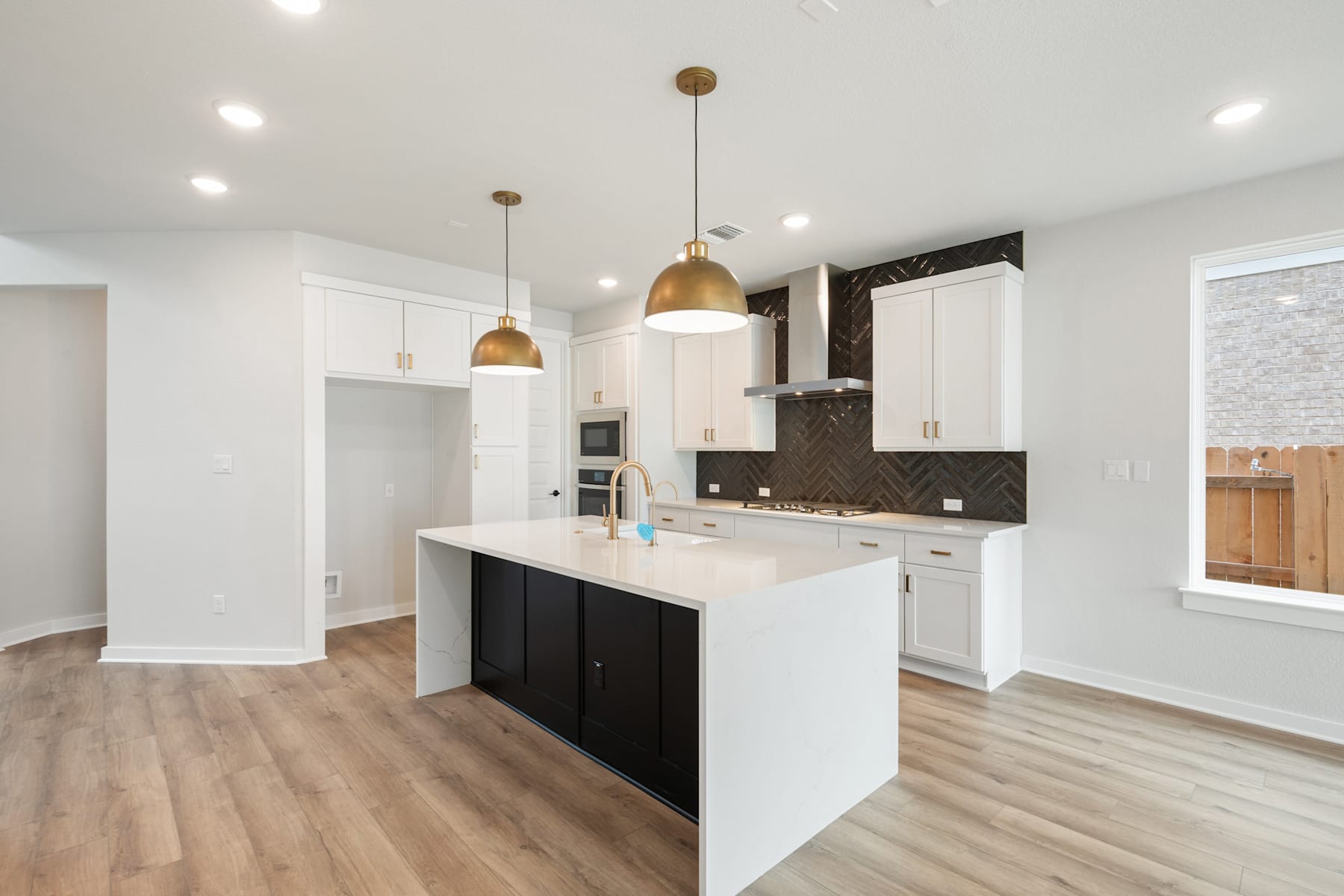 A modern, open-concept kitchen with white cabinets, a black island, and gold pendant lights, set against a backdrop of hardwood floors and a bright, airy space.