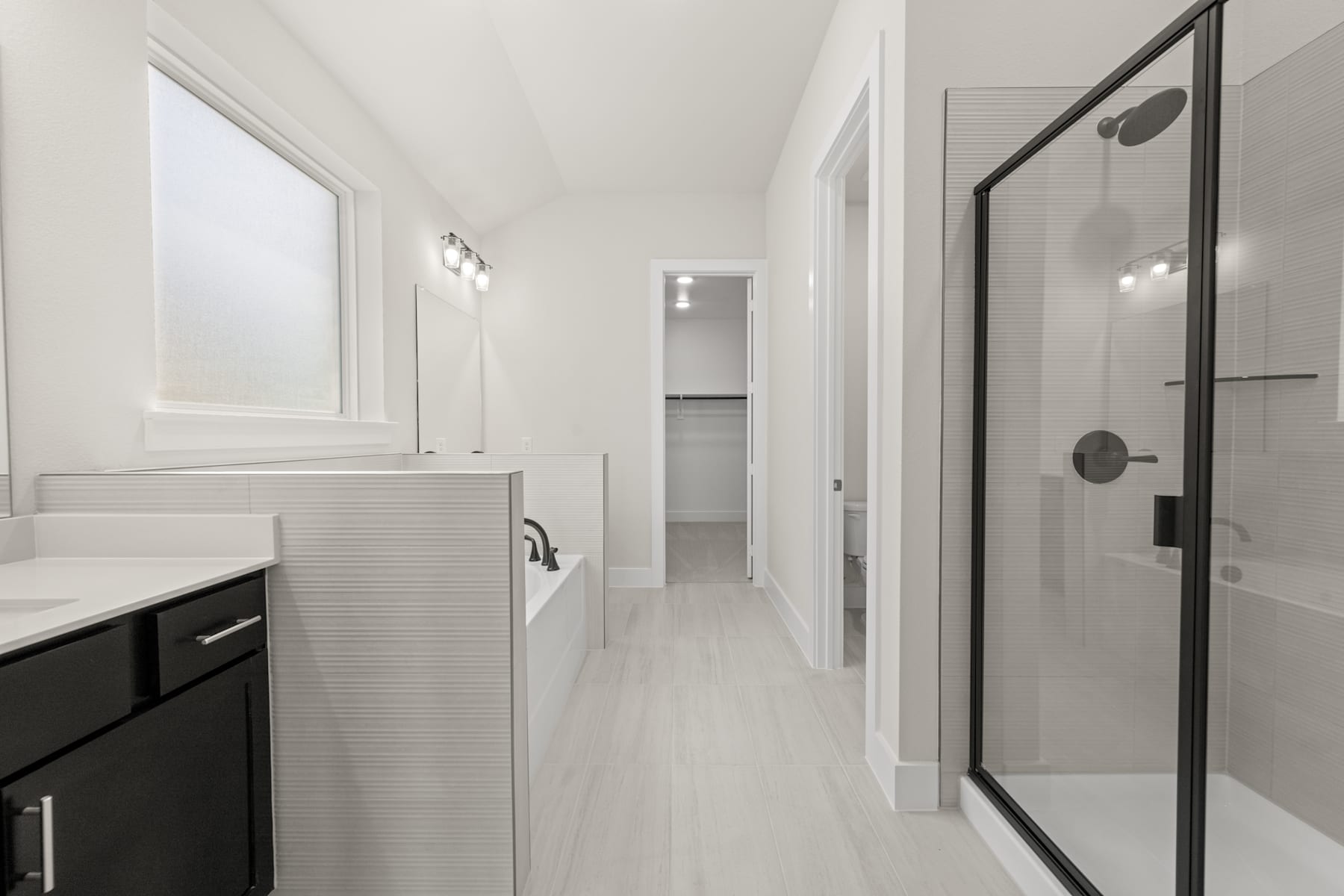 A modern, minimalist bathroom with a black vanity, a large mirror, and a glass-enclosed shower visible in the background.