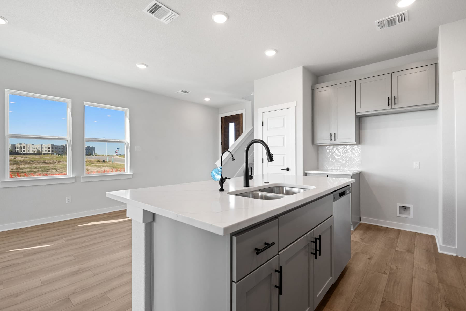 A modern, well-lit kitchen with white cabinets, a stainless steel sink, and a large window overlooking a scenic outdoor landscape.