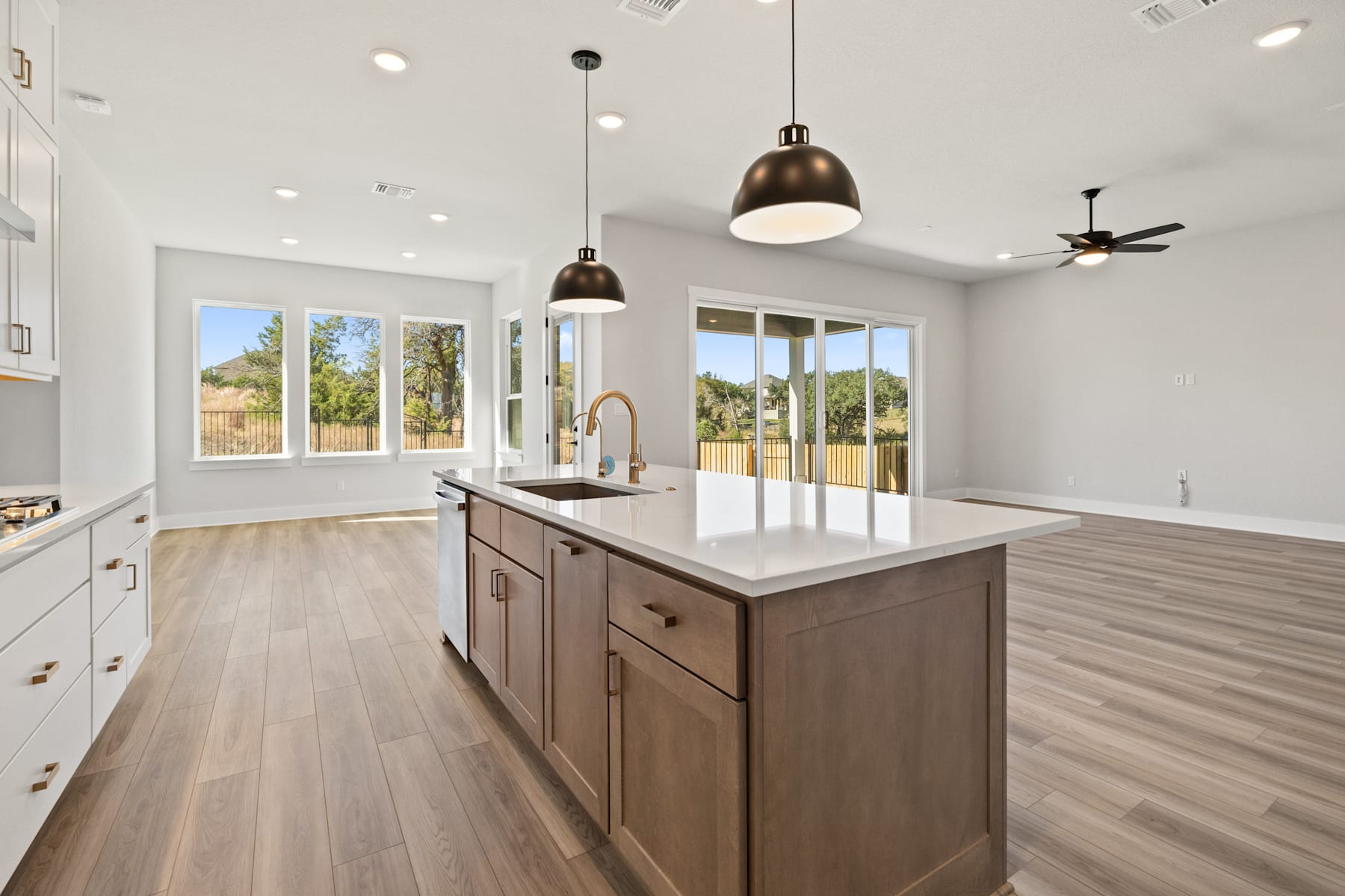 A modern, open-concept kitchen with a large island, wooden cabinets, and pendant lighting, set against a backdrop of large windows overlooking a scenic outdoor area.