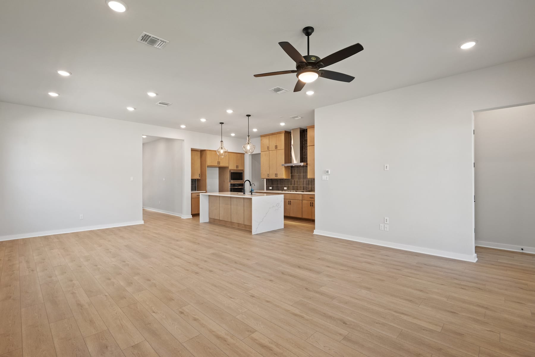 A spacious, open-concept living area with a modern kitchen, hardwood floors, and a ceiling fan, creating a bright and inviting atmosphere.