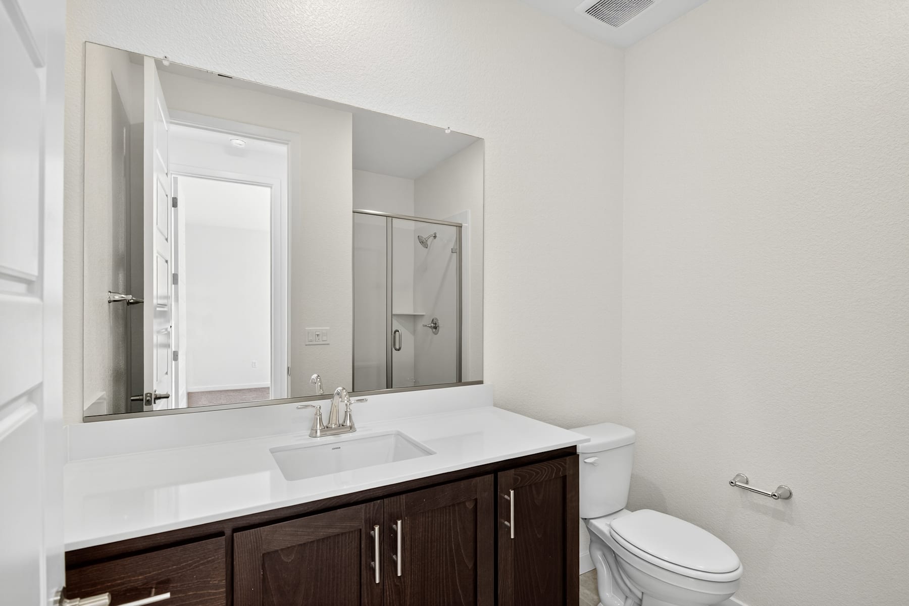 A modern and minimalist bathroom with a dark wood vanity, a white sink, and a large mirror on the wall.