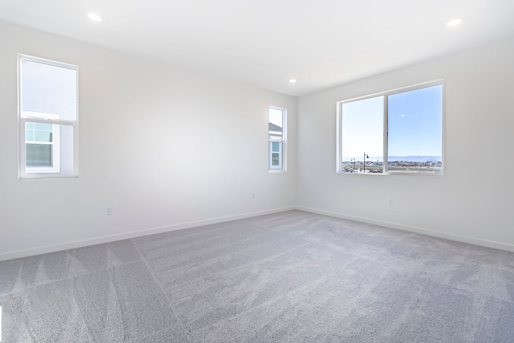 A bright, spacious room with large windows offering a view of the outdoors, featuring a clean and minimalist design with hardwood flooring.