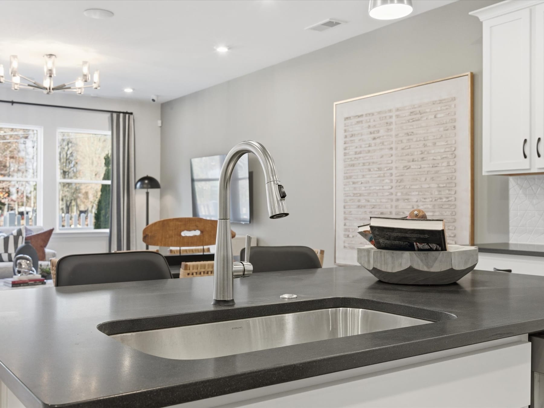 A modern and stylish kitchen with a stainless steel sink, dark countertops, and a brick wall in the background, along with various decorative elements and appliances.