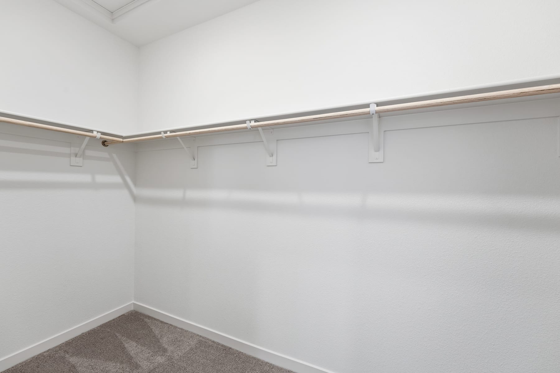 A white, empty closet with a metal clothing rod and hangers, set in a corner of a room with gray carpeting.