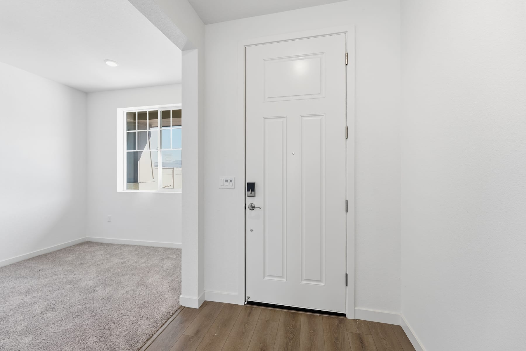 A bright, minimalist room with a white door, hardwood flooring, and a window providing natural light.