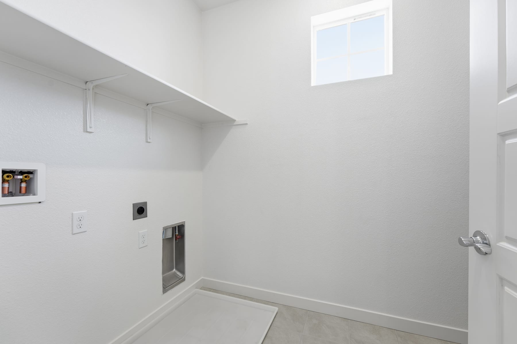 A bright, minimalist interior space with a high ceiling, a small window, and a simple wall-mounted shelf.