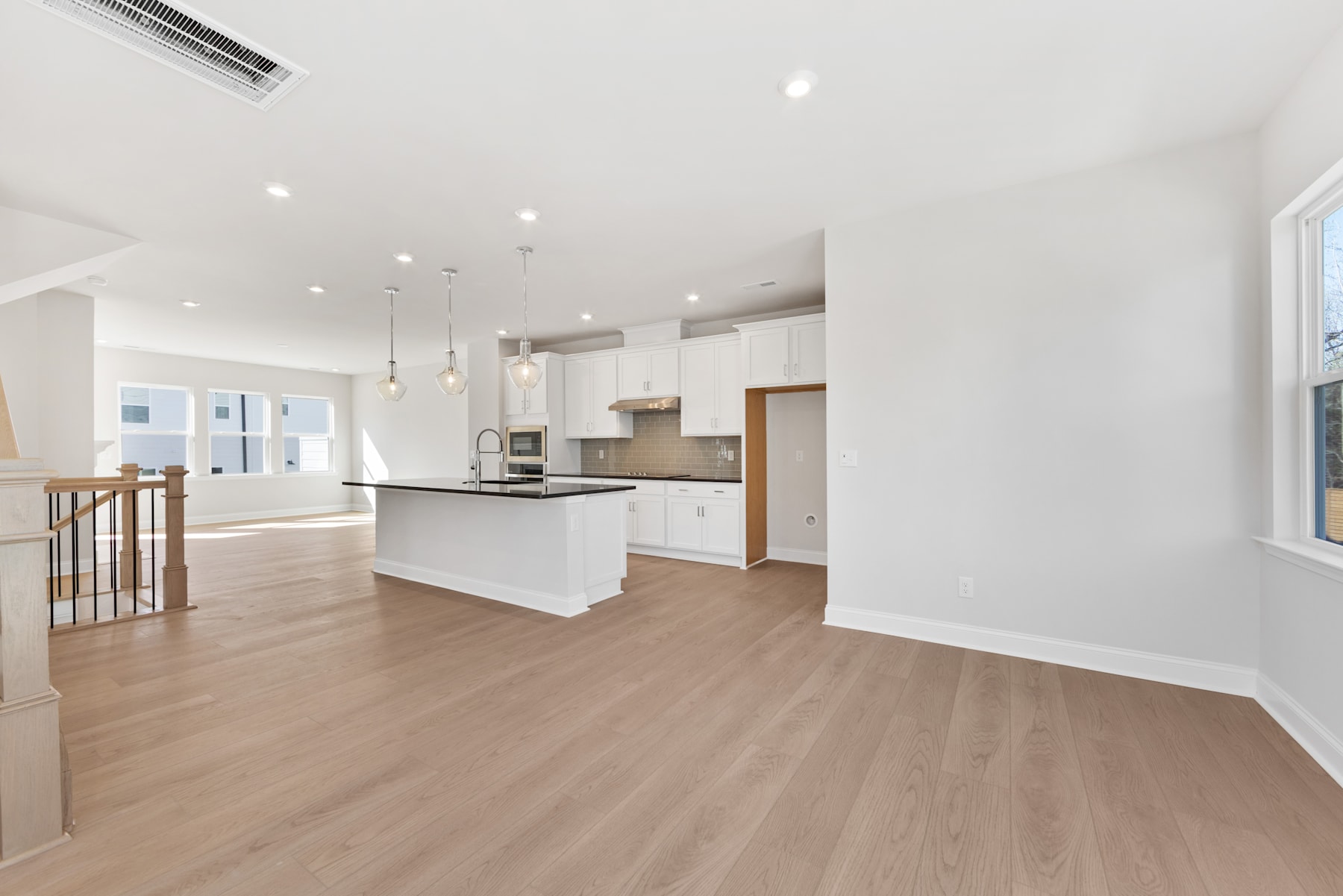 A modern, open-concept kitchen and living space with white walls, hardwood floors, and a central island.