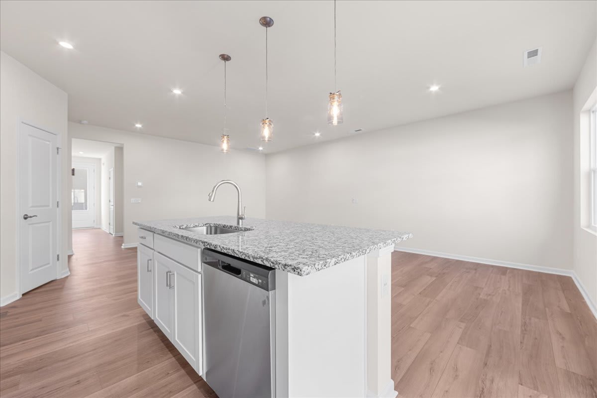 A modern, minimalist kitchen with white walls, a granite countertop, and a stainless steel appliance in the foreground, set against a hardwood floor in the background.