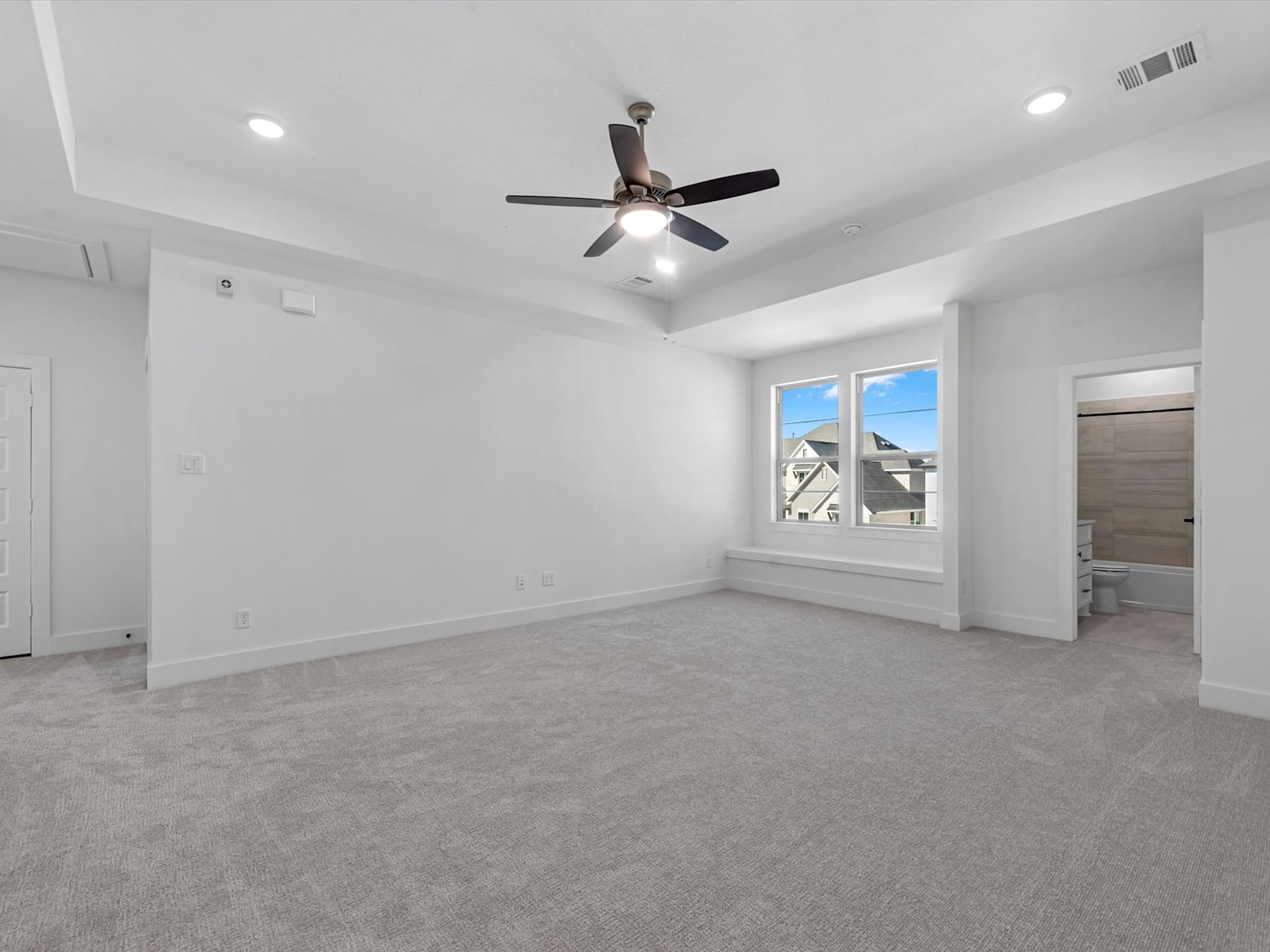 A spacious, well-lit room with a ceiling fan and a window overlooking the exterior of the building.