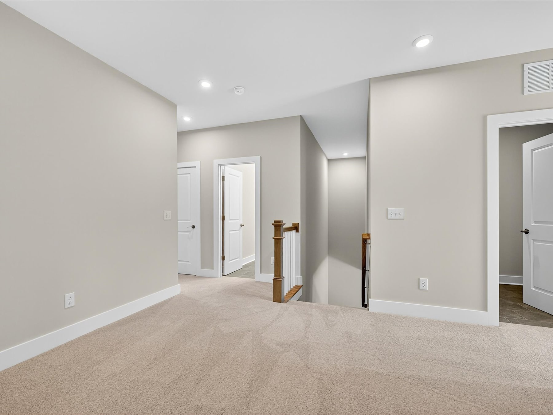 A spacious, well-lit room with light-colored walls, hardwood floors, and multiple doorways leading to other areas of the home.