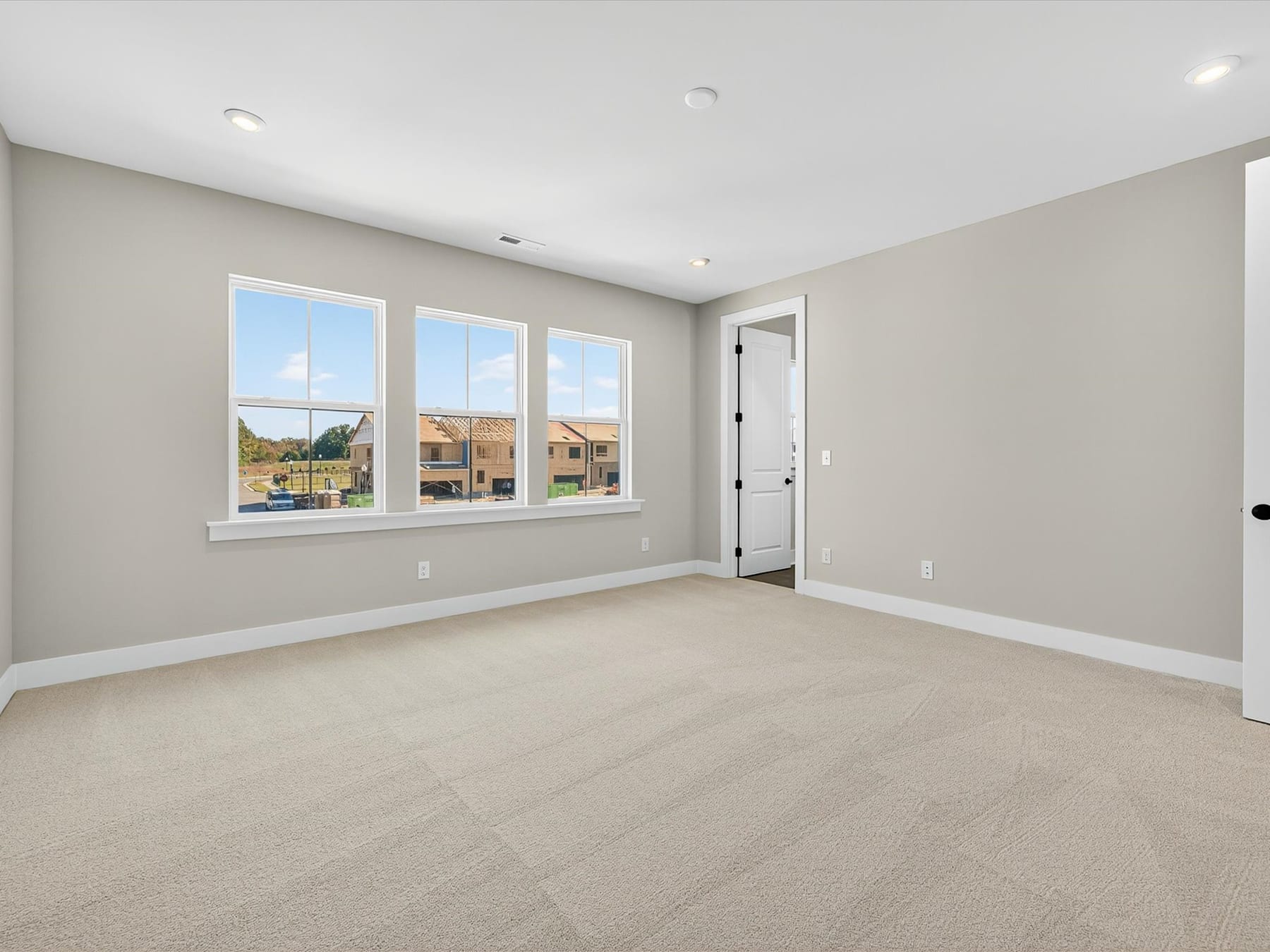 An empty, spacious room with large windows overlooking a residential neighborhood in the background.