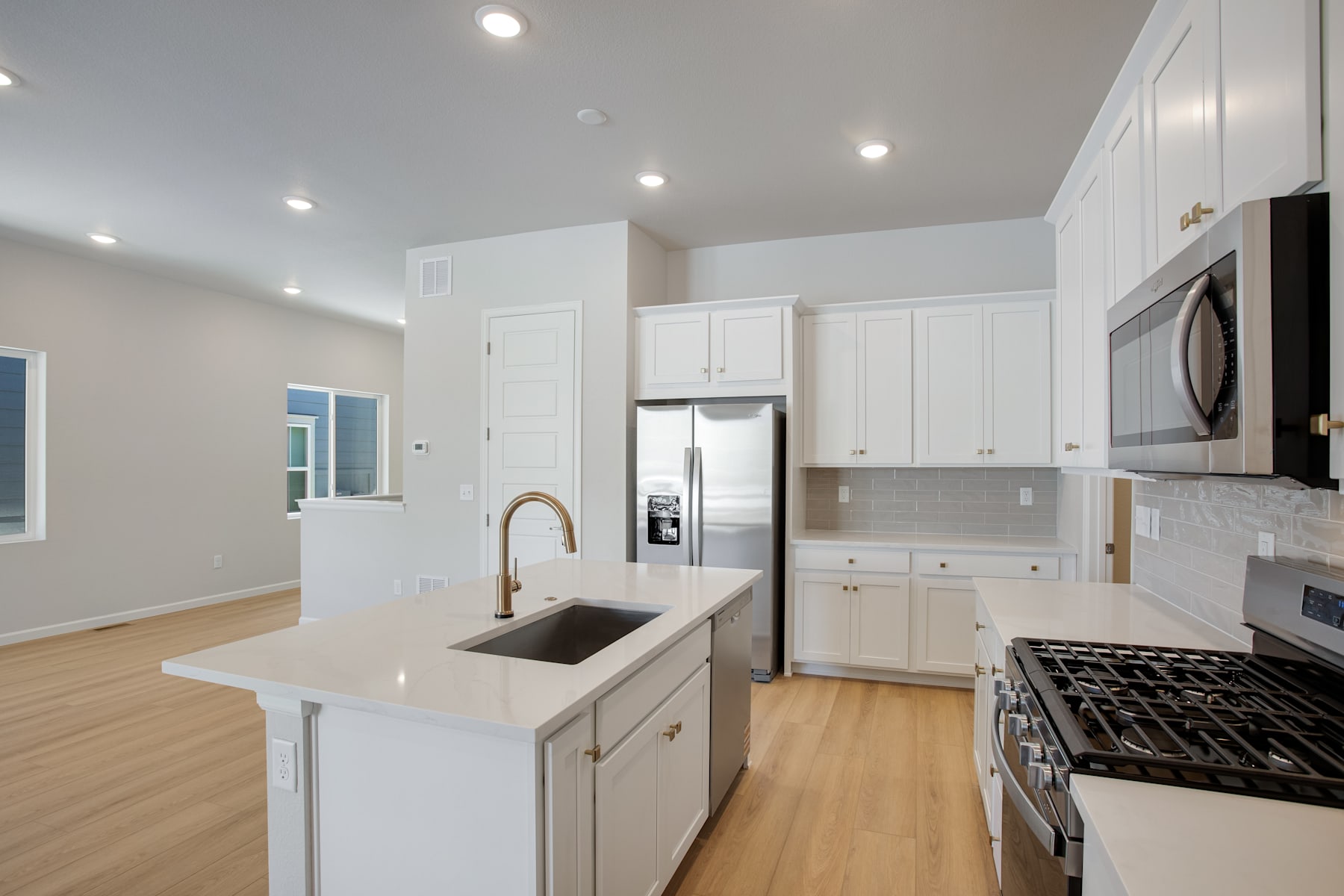 A modern, well-lit kitchen with white cabinets, stainless steel appliances, and a hardwood floor.