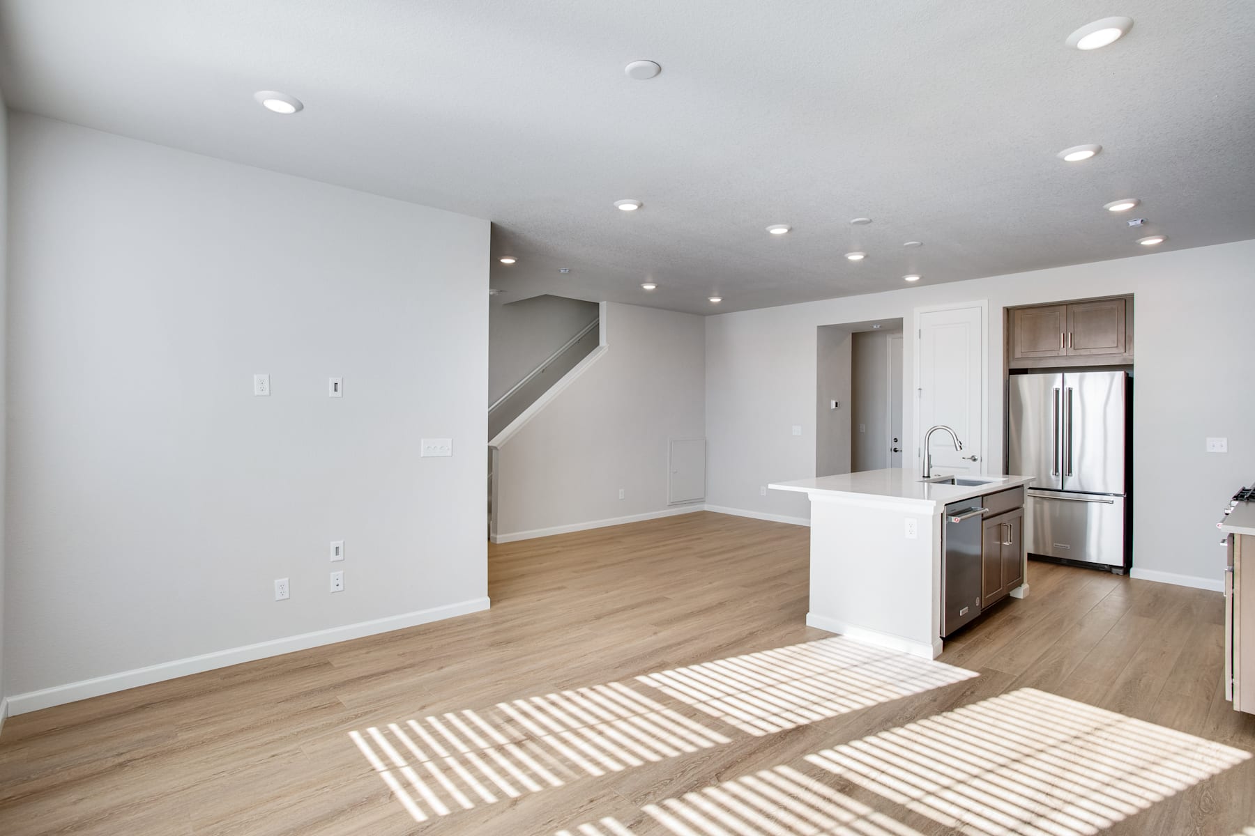 A spacious and modern open-plan living area with a kitchen, hardwood floors, and natural lighting streaming in through the windows.