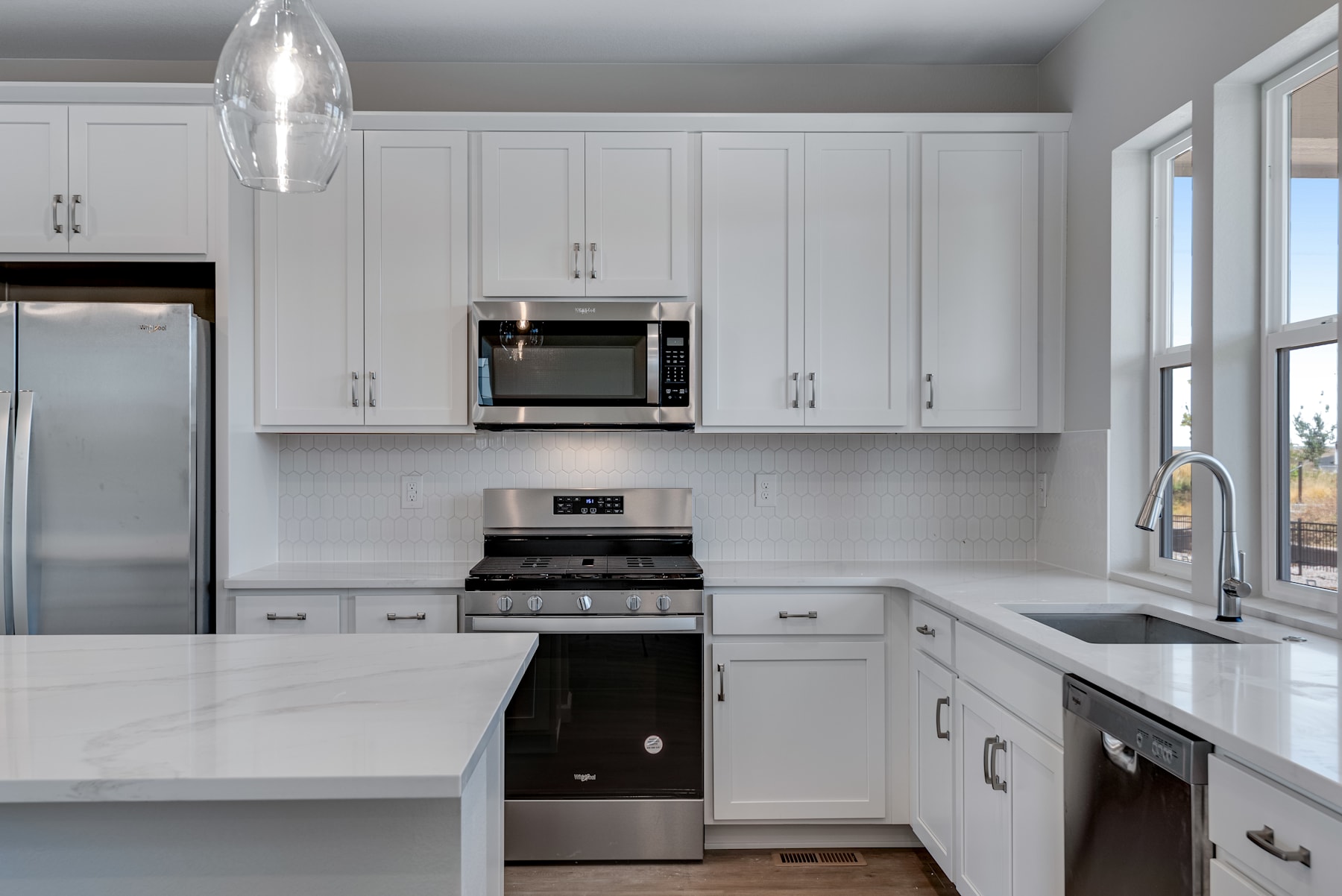 A modern, well-lit kitchen with white cabinets, stainless steel appliances, and a large window providing natural light.