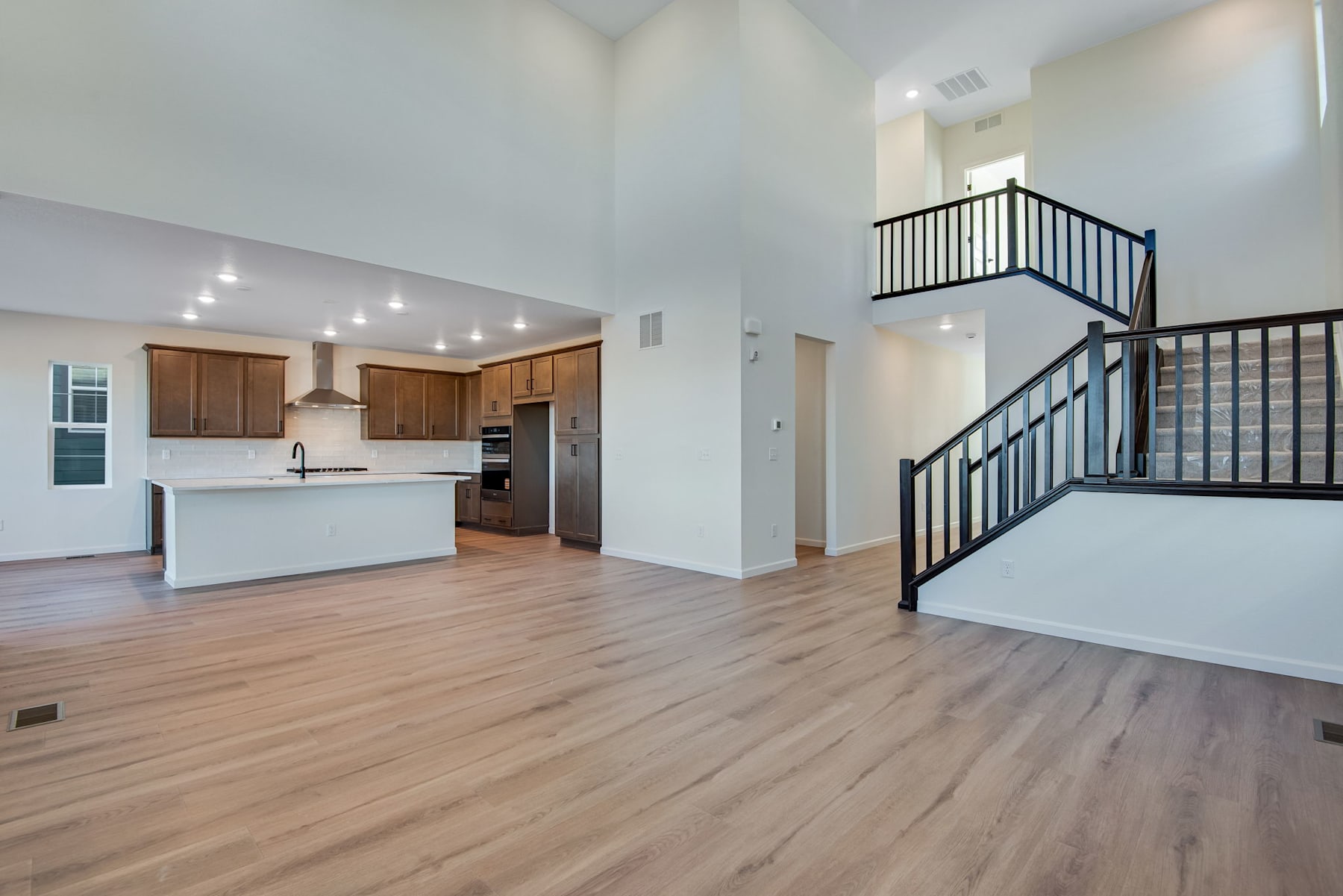 A spacious and modern open-plan living area with a kitchen, hardwood floors, and a staircase leading to an upper level.