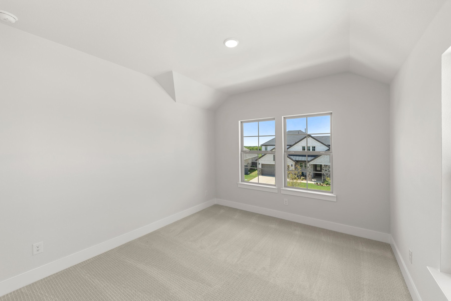 A bright, spacious room with large windows overlooking a residential neighborhood, featuring a clean, minimalist design with white walls and a light-colored floor.