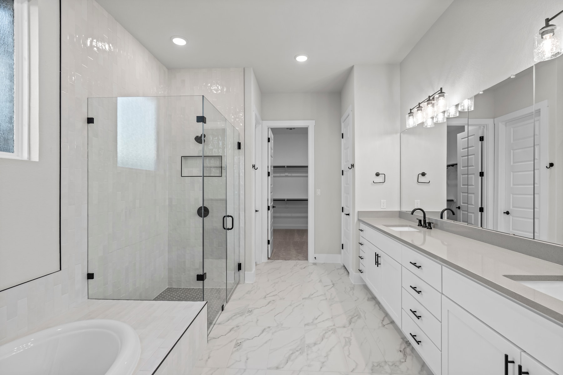 A spacious and modern bathroom with a glass-enclosed shower, white cabinets, and a marble-like floor.