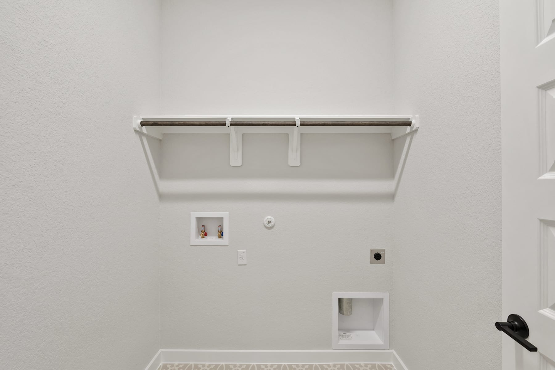 A white wall with a metal shelf and electrical outlets, creating a minimalist and clean-looking space.