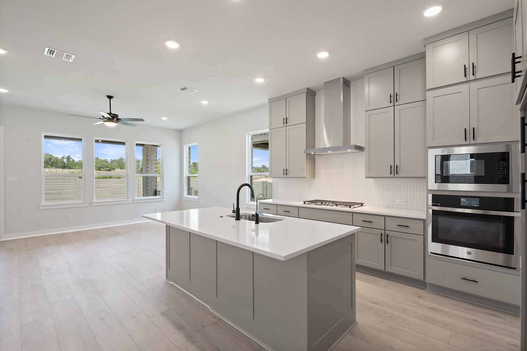 A modern, open-concept kitchen with gray cabinets, white countertops, and stainless steel appliances, set against a backdrop of large windows overlooking a scenic outdoor view.