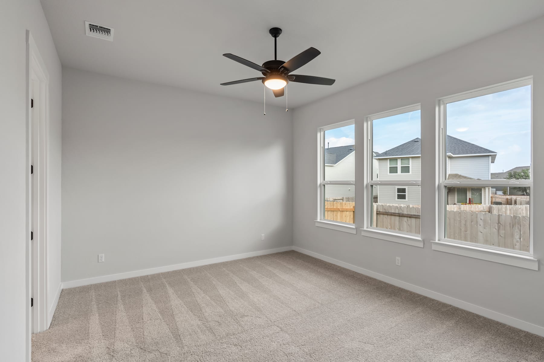 An empty room with a ceiling fan, large windows, and a hardwood floor.